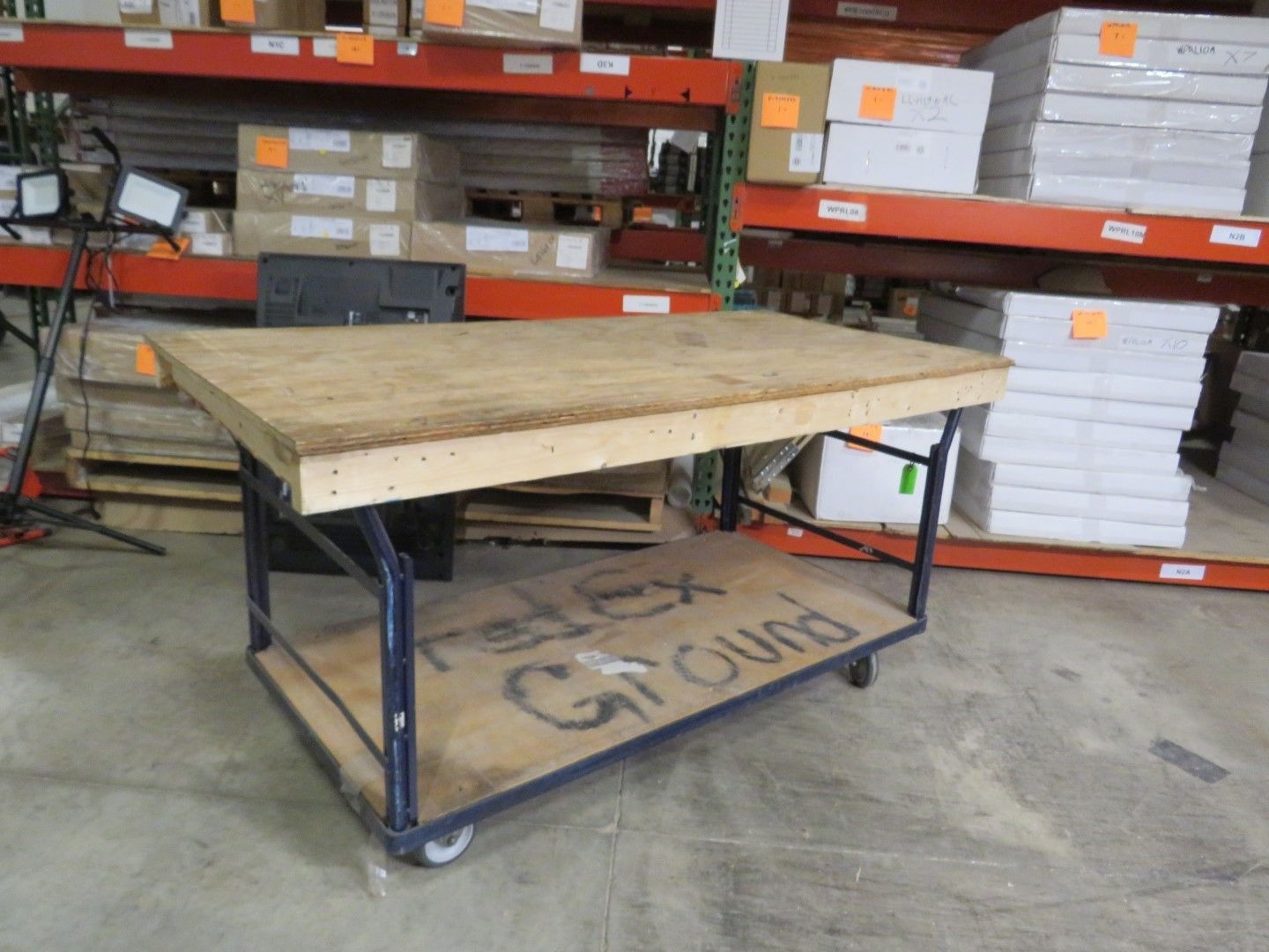 A rolling workbench with plywood shelves in a warehouse.