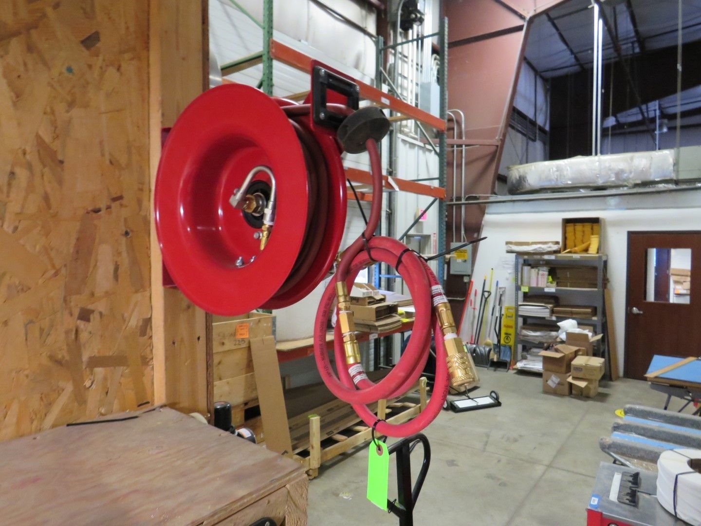 Red hose reel mounted on a wall in a warehouse. Red hose hangs down.