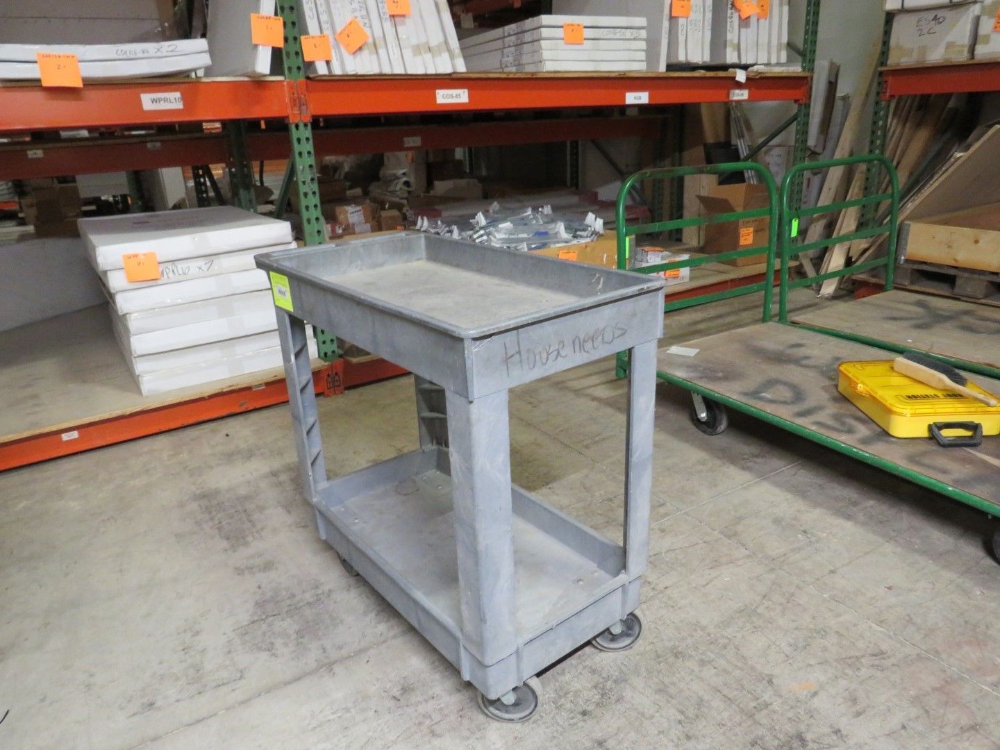 Gray utility cart with two shelves and four wheels, in a warehouse setting.