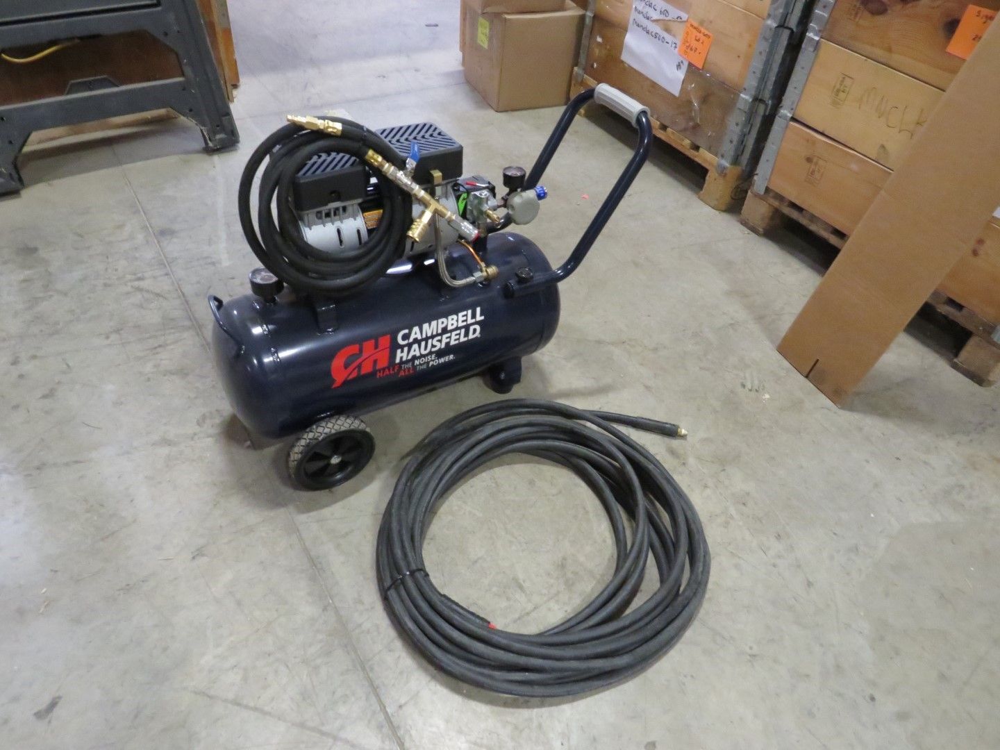 Black air compressor with hose and handle, sitting on a concrete floor.