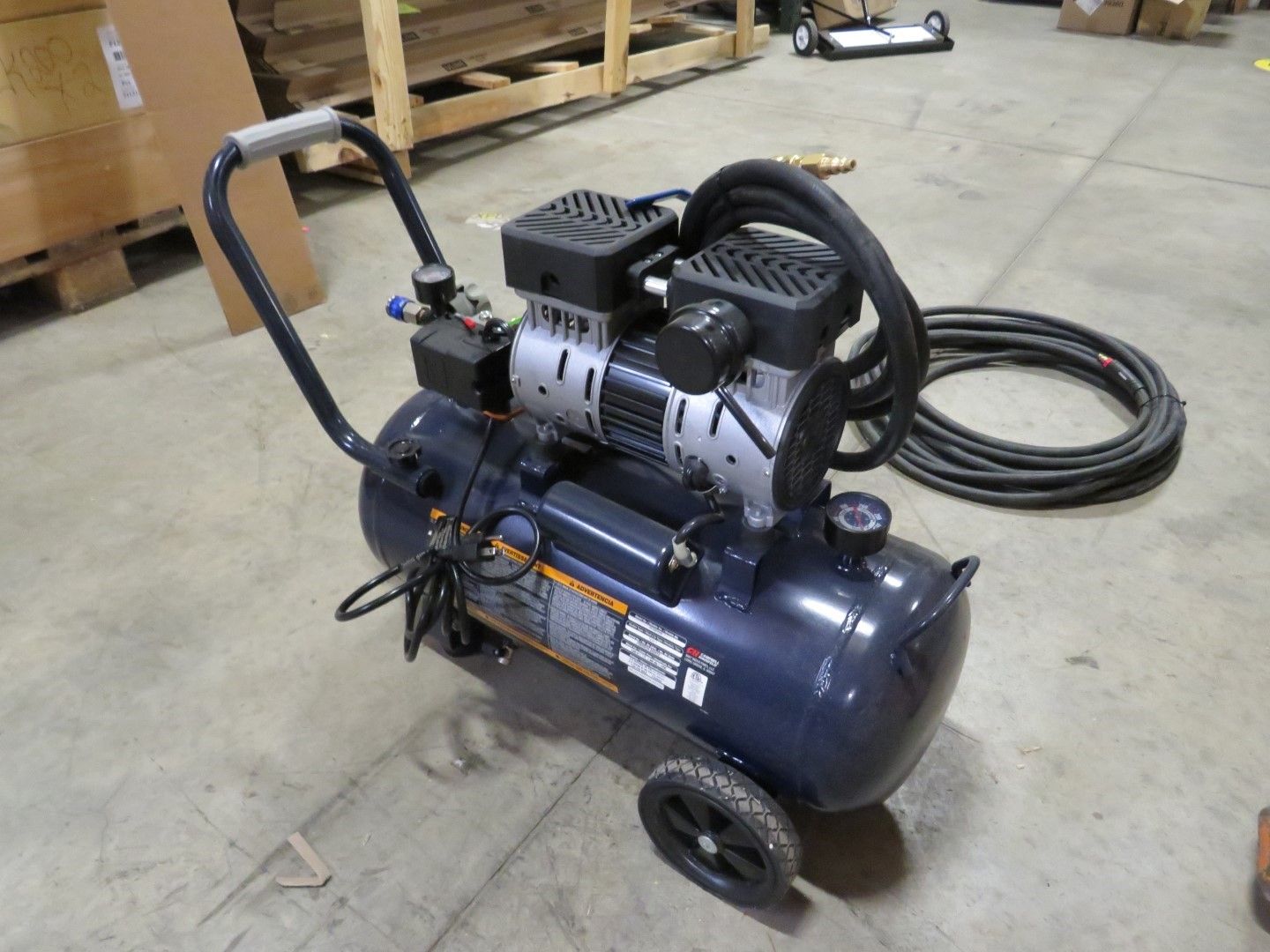 Blue air compressor with black handle, wheels, and hose, indoors.
