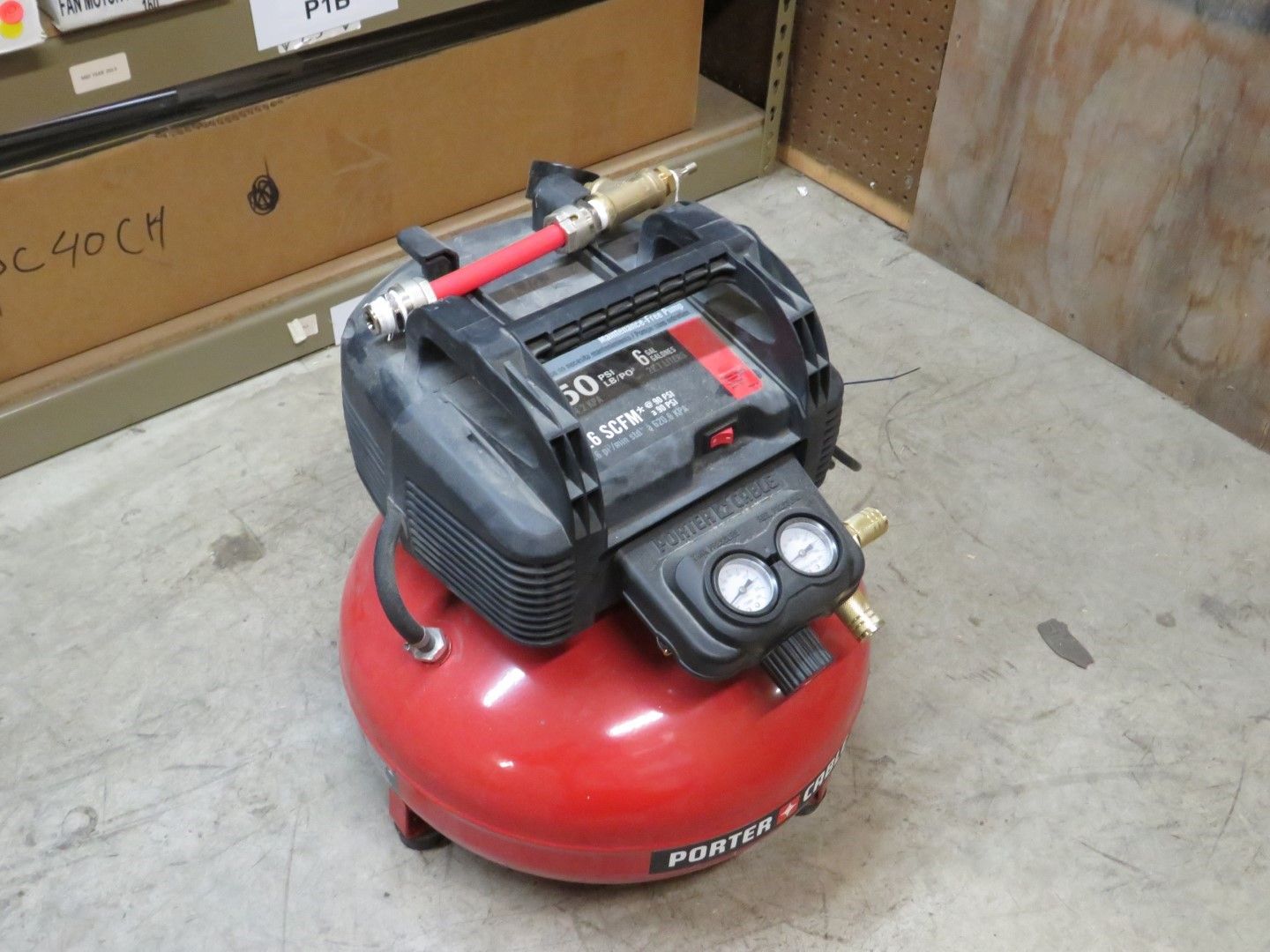 Red and black air compressor on a concrete floor.