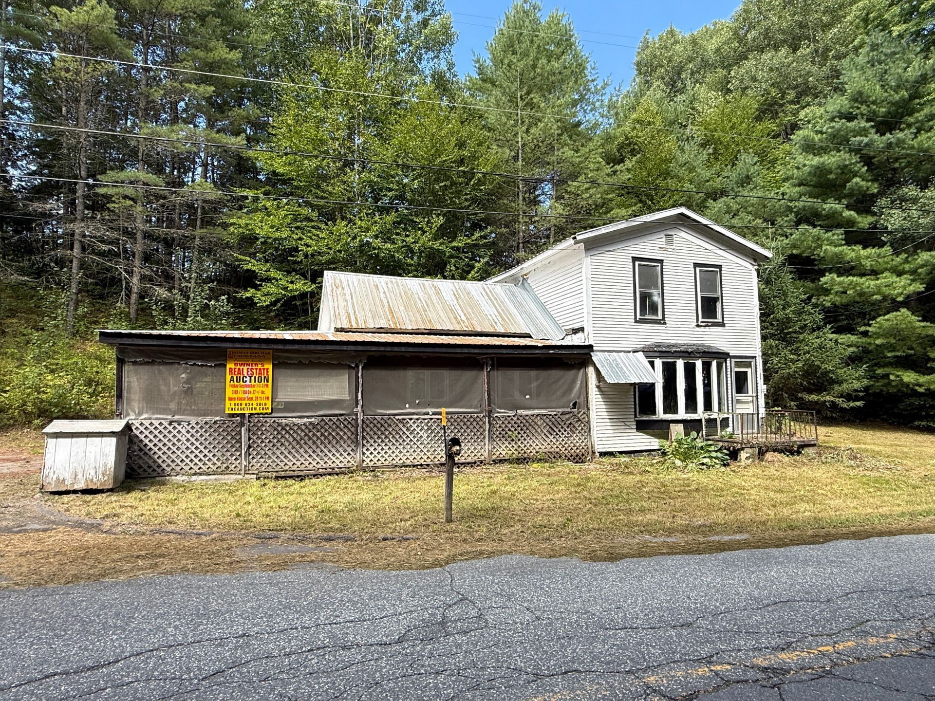rural house and barn beside a road, with siding and trees in the background