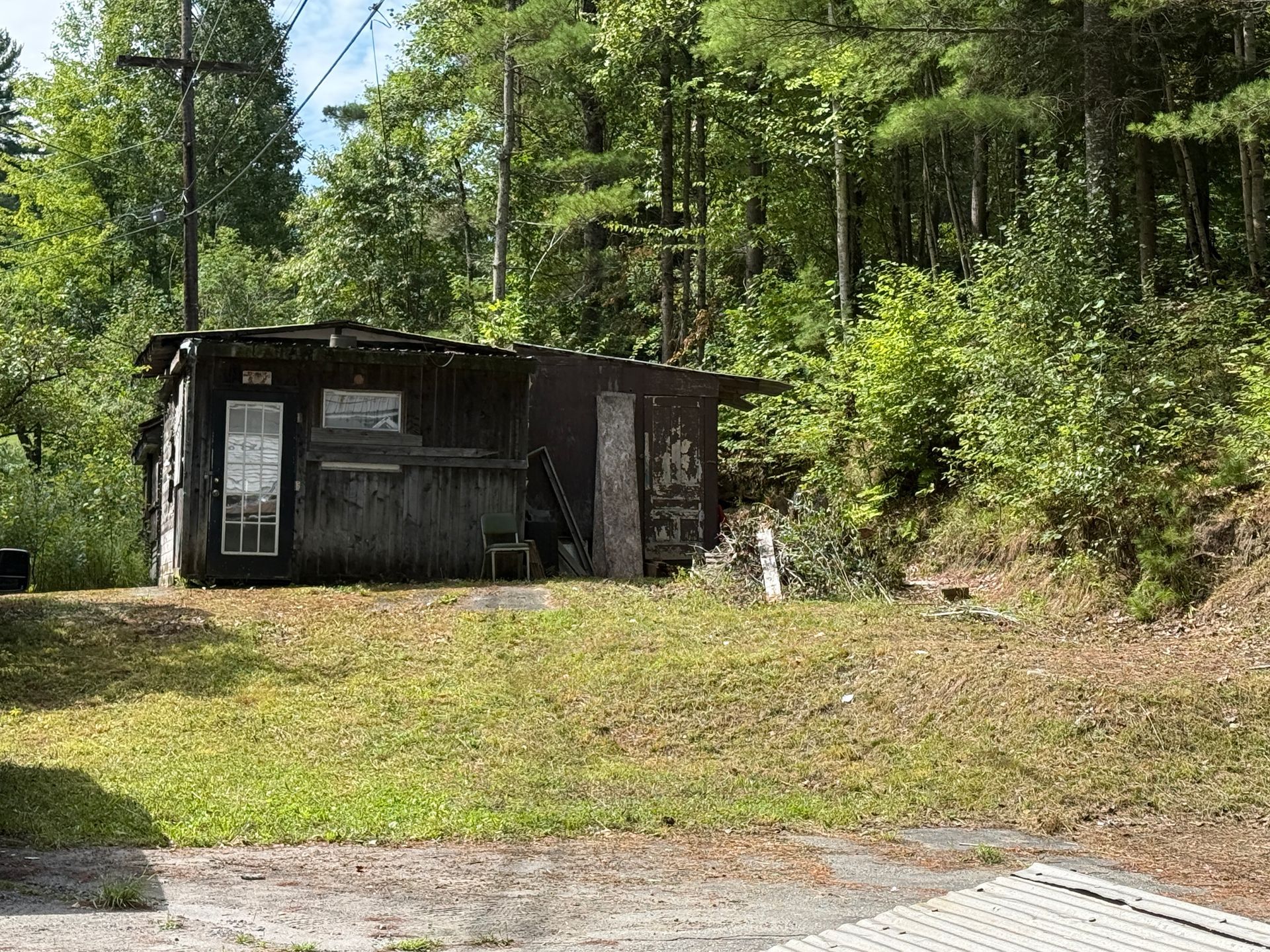 Small dark cabin beside a grassy clearing in a wooded area