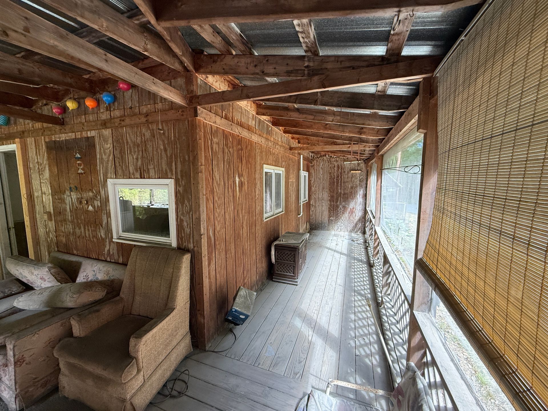 Rustic wooden porch with woven walls, benches, and a long walkway overlooking greenery