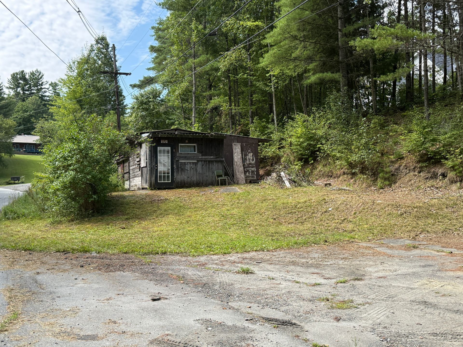 Small shed beside a grassy roadside clearing, surrounded by trees and brush.
