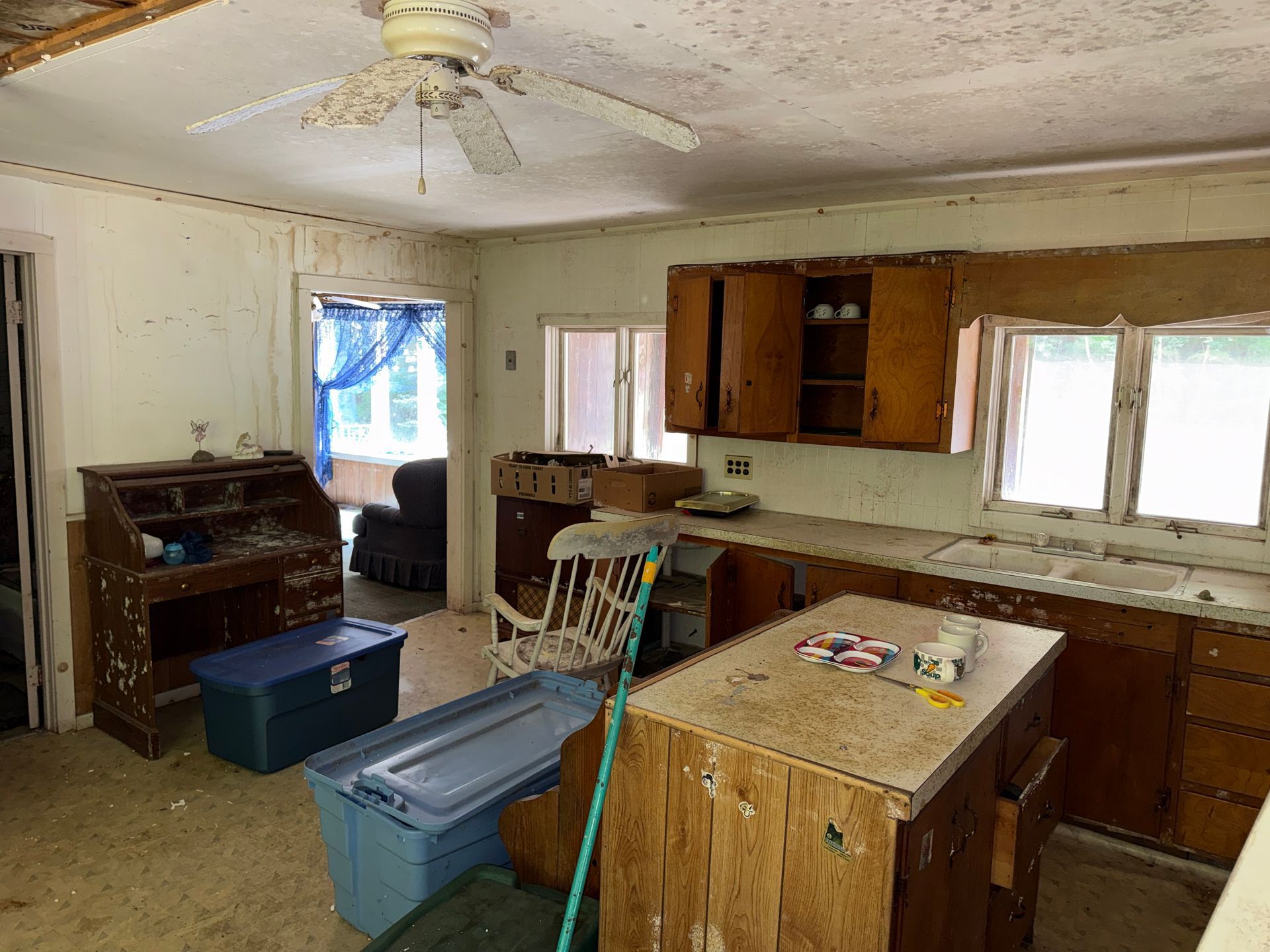  kitchen with worn cabinets, plastic bins, and ceiling fan