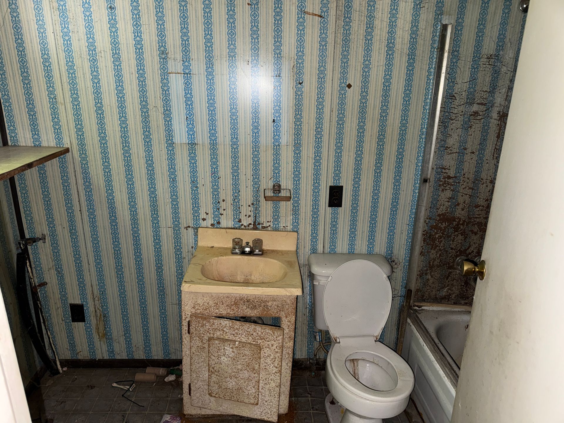 Small bathroom with striped wallpaper, sink vanity, toilet, and bathtub with shower curtain.
