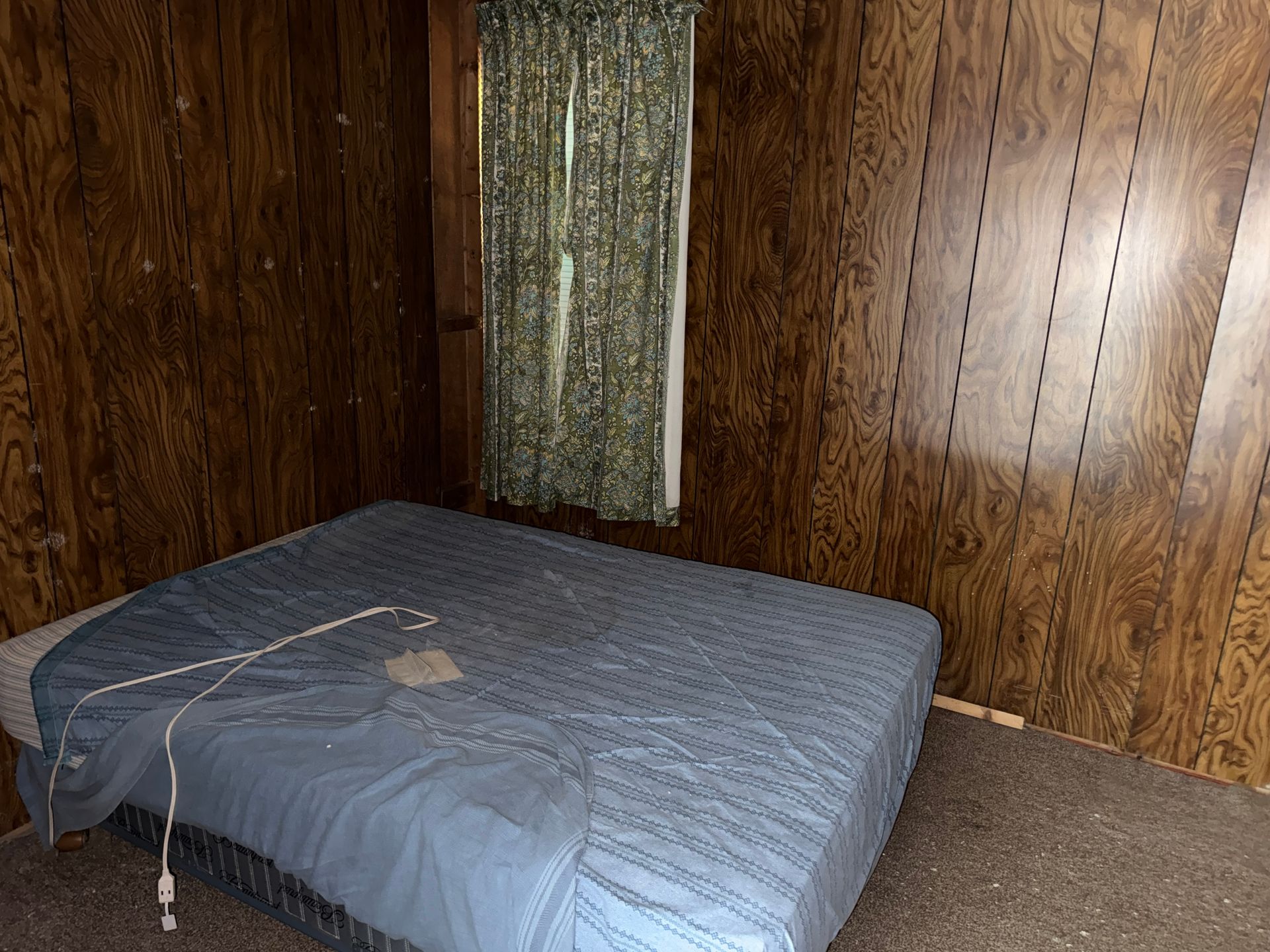 Empty bedroom with a blue mattress on the floor, wood-paneled walls, and carpeted floor.