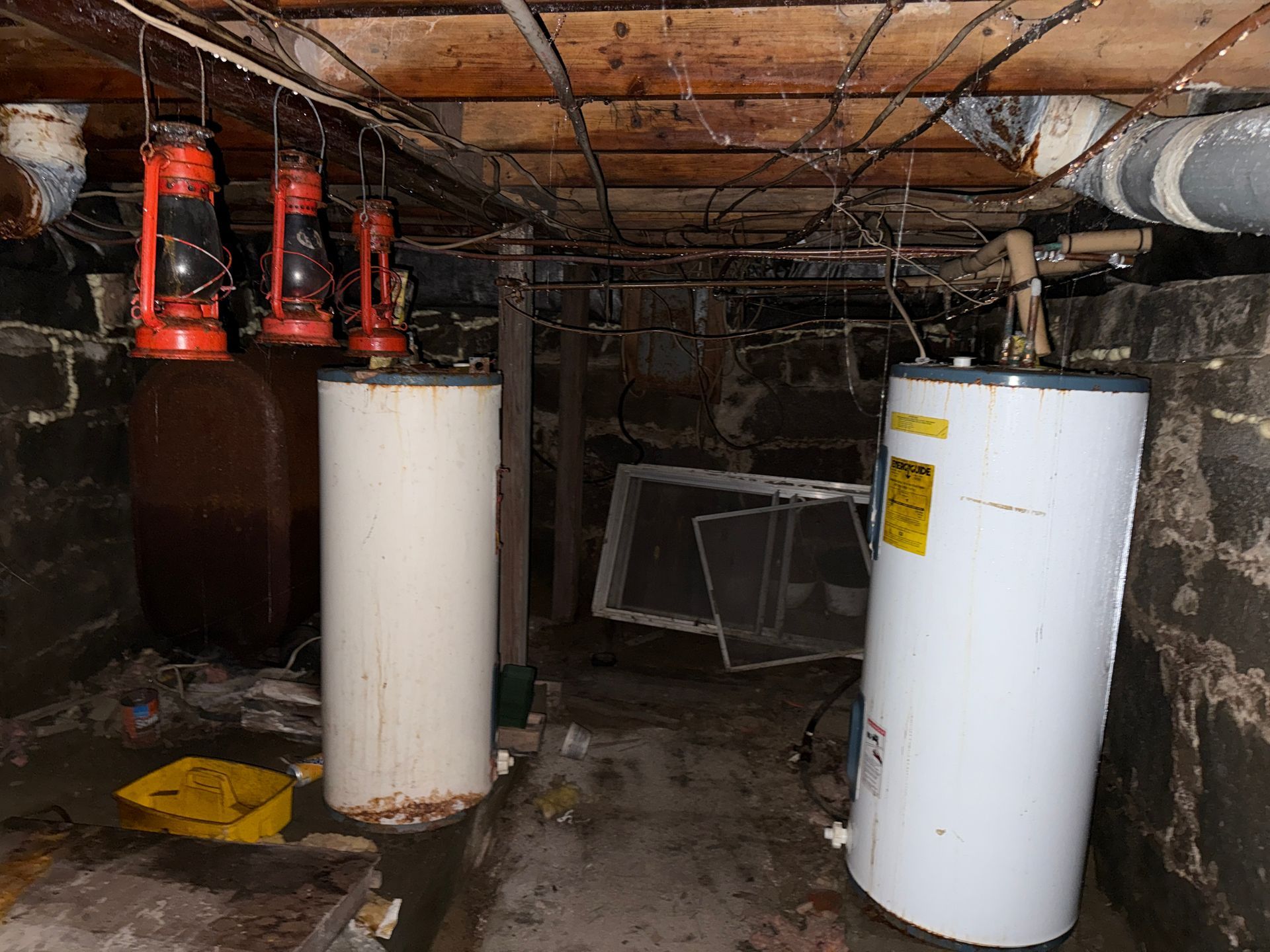Basement utility area with water heaters, pipes, and exposed ceiling beams.