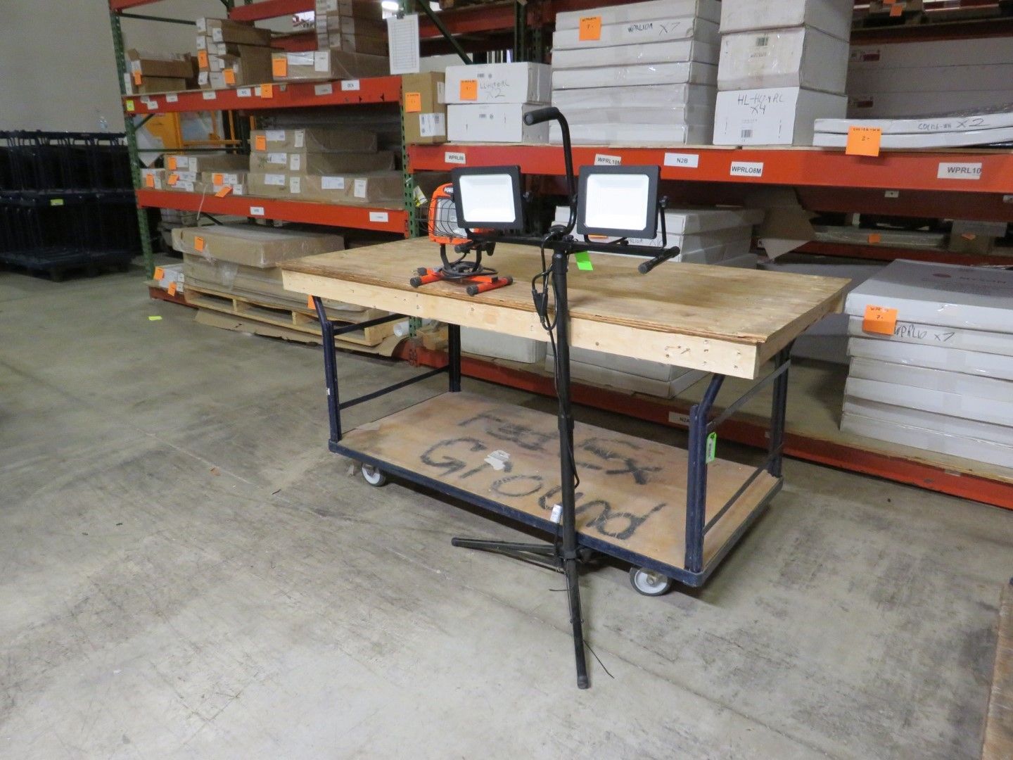 A work cart with two floodlights sits in a warehouse.