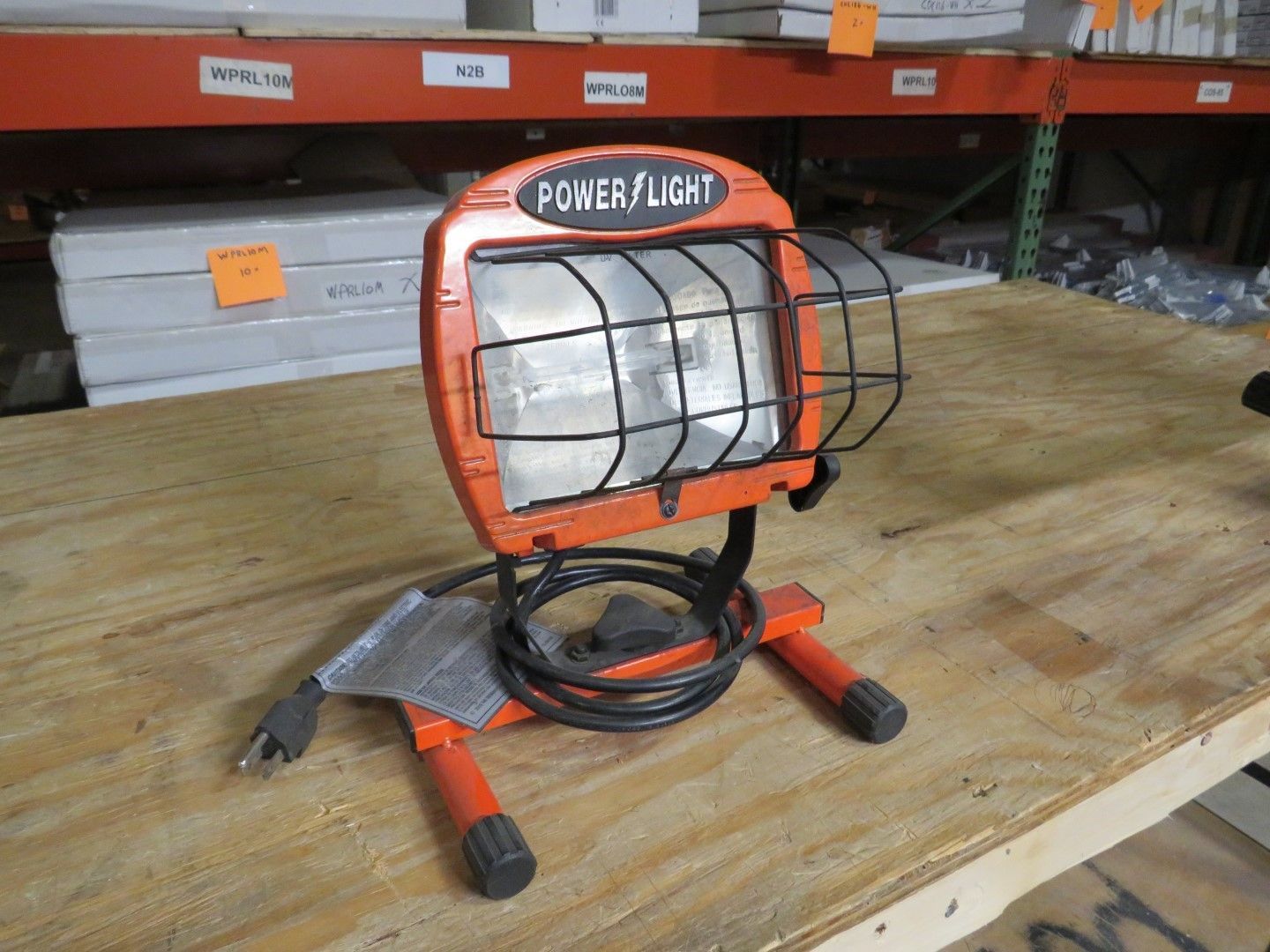 Orange Power Light work lamp on a wooden surface, with a black cord and metal cage.