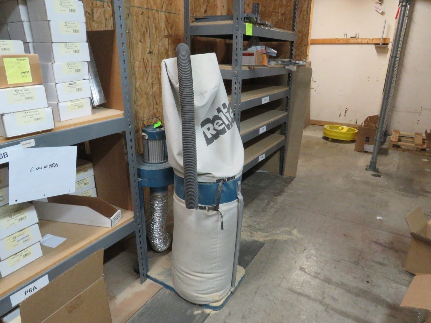Dust collector with bag, next to shelving in a workshop.