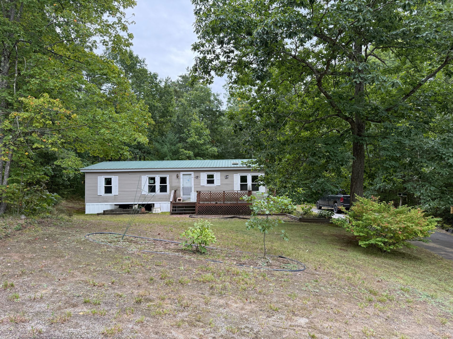 White mobile home in a wooded yard with a gravel driveway and trees surrounding it