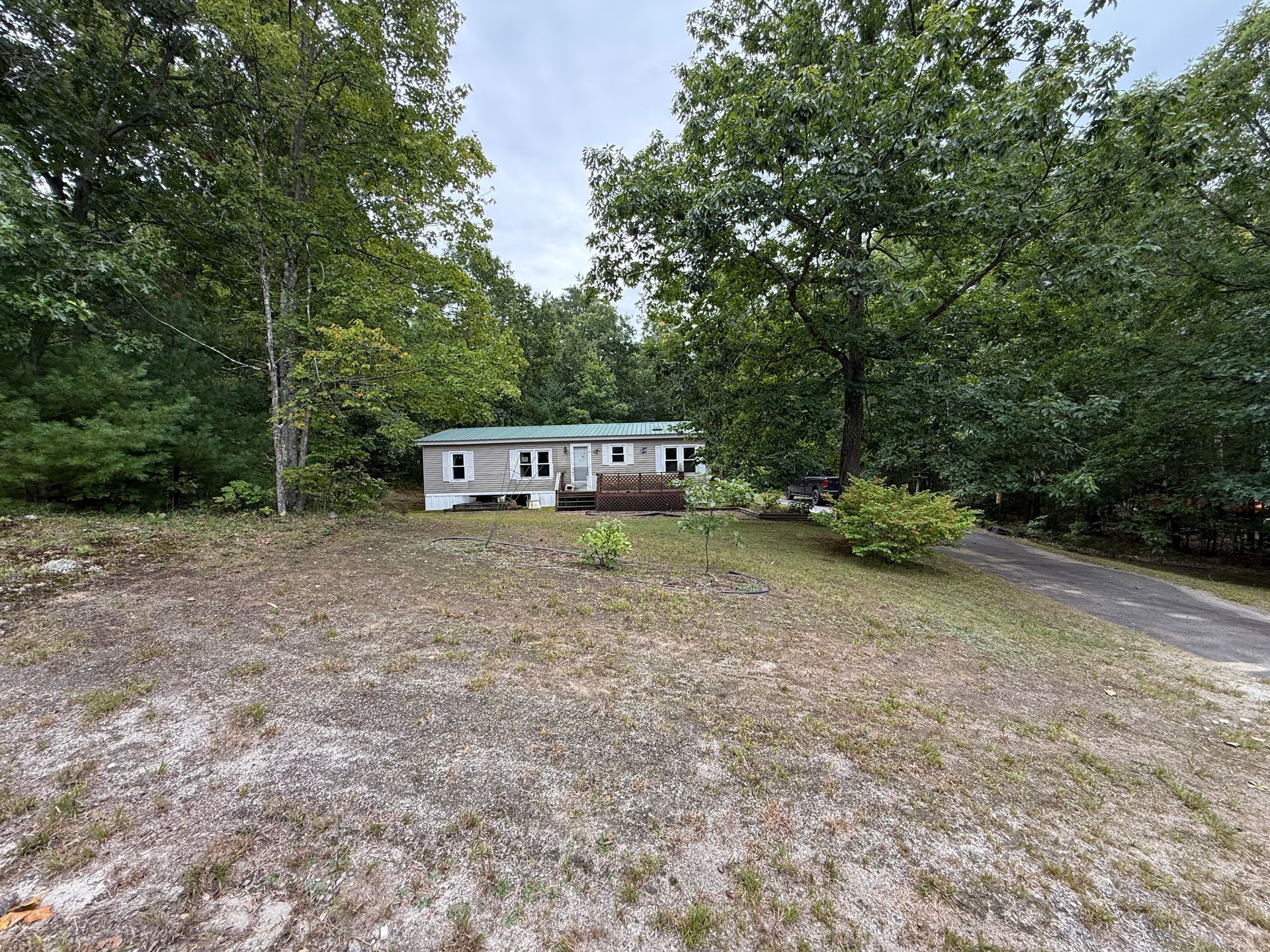 Small house with white siding and brick front, set back in a wooded yard with a gravel driveway.