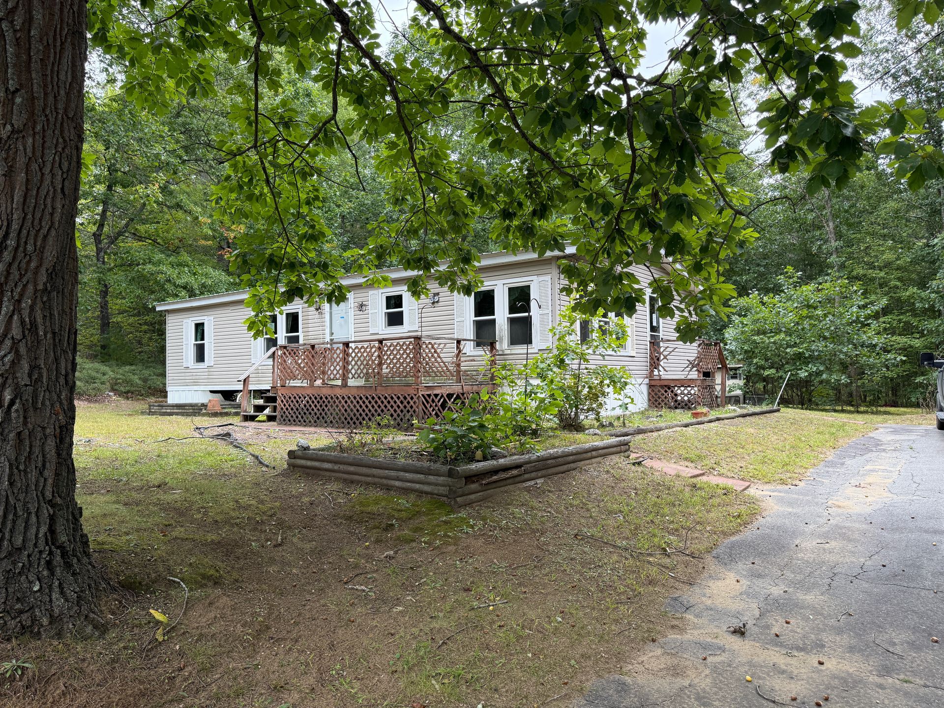 Small white house with a wooden porch on a wooded lot beside a gravel driveway