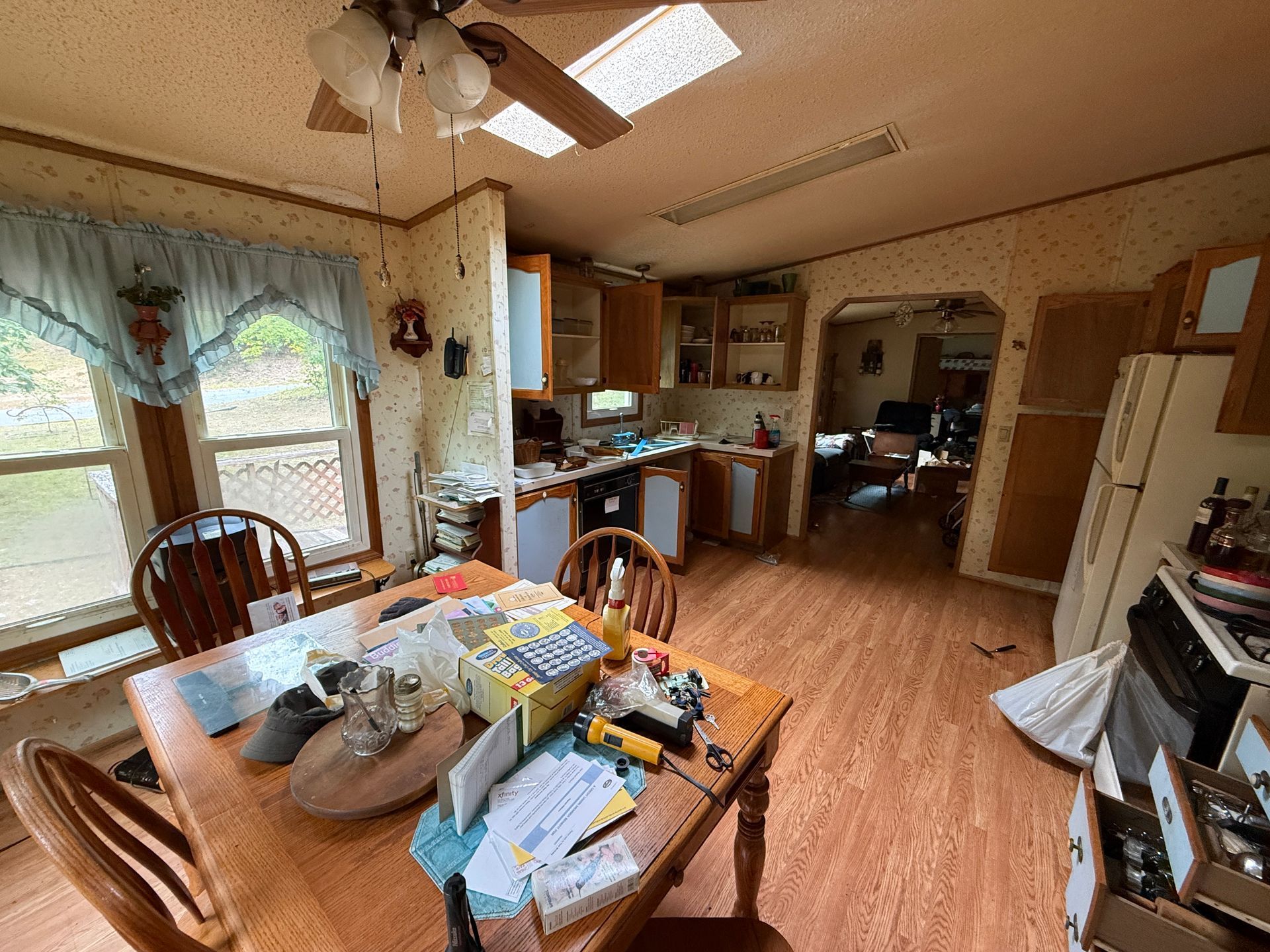 Cozy kitchen and dining area with wood floors, table with items, and a window with light curtains.