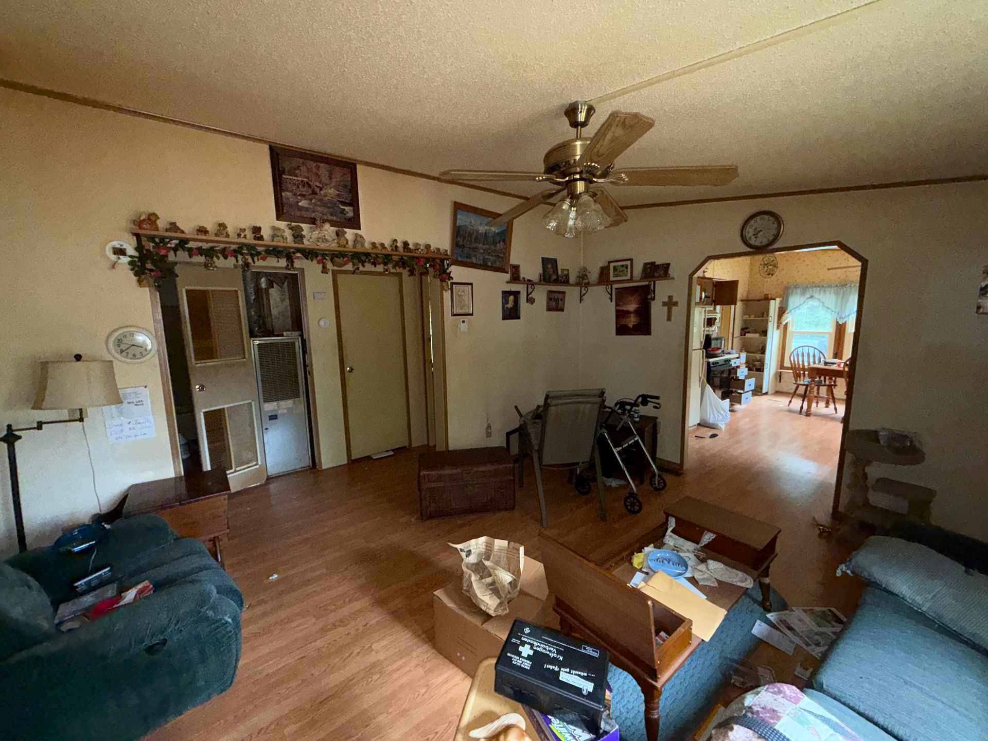 living room with wood floor, ceiling fan, couches, and doorway to a bright kitchen