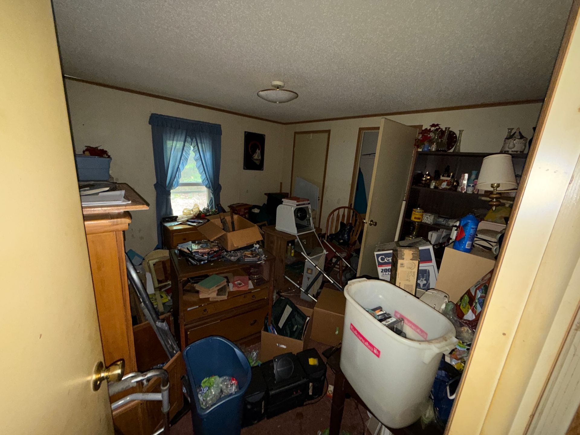 bedroom with furniture, boxes, and a bicycle near a window with blue curtains