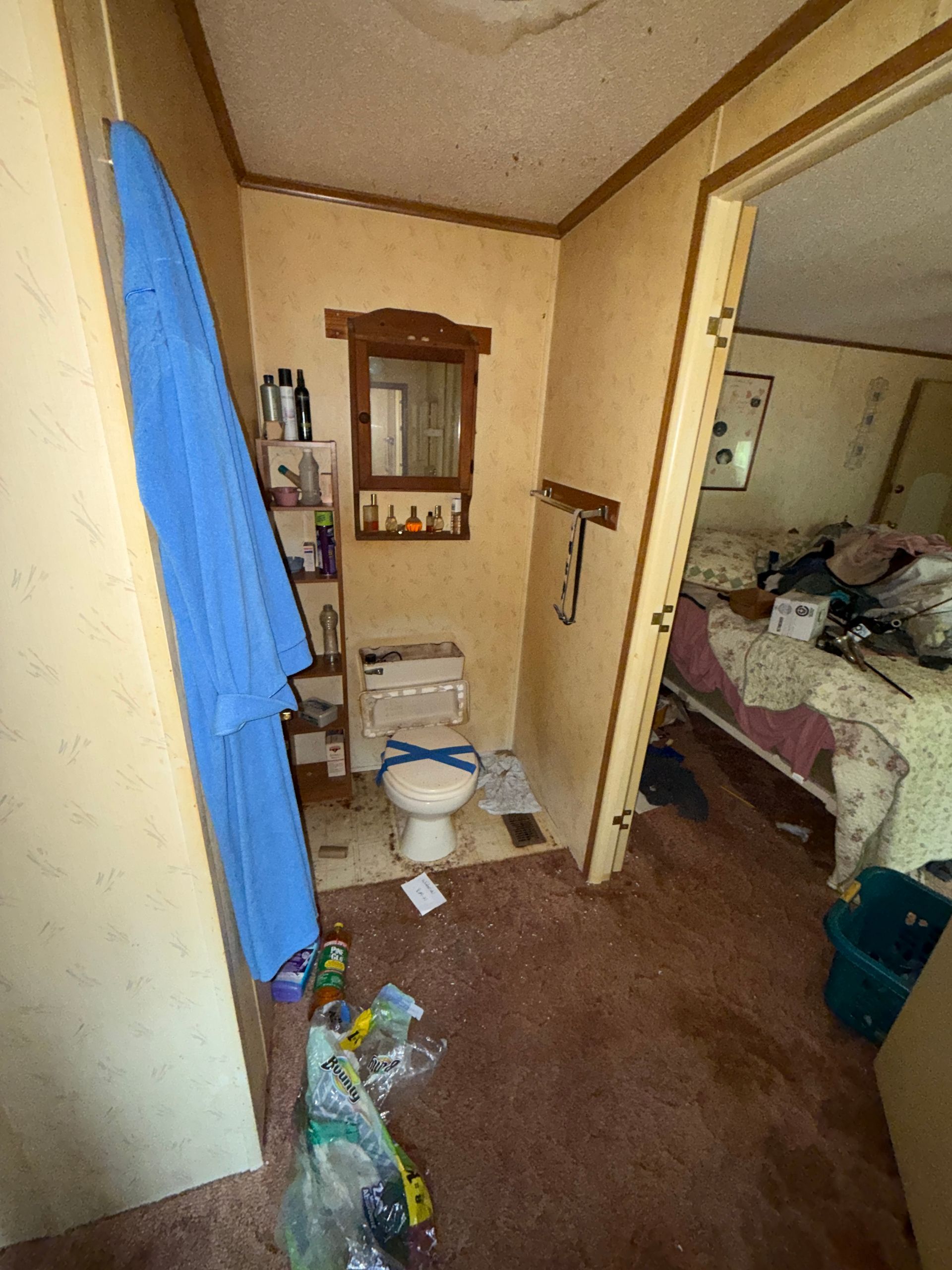 Narrow hallway with a toilet, blue towel, and doorway leading to a bedroom on the right.