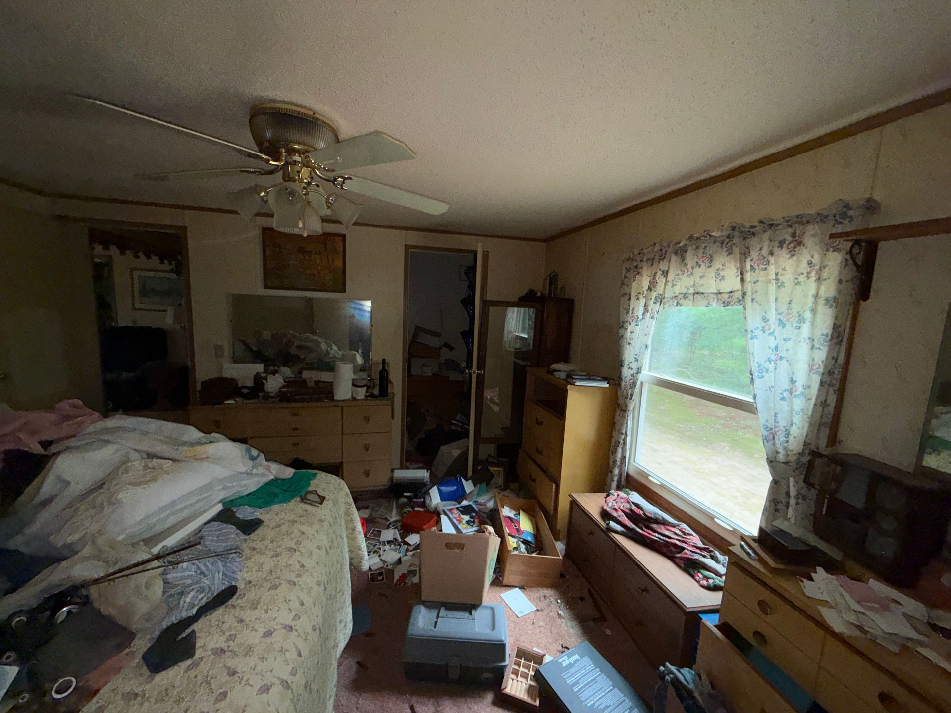 bedroom with bed, dresser, open boxes, and sunlight through a window with curtains