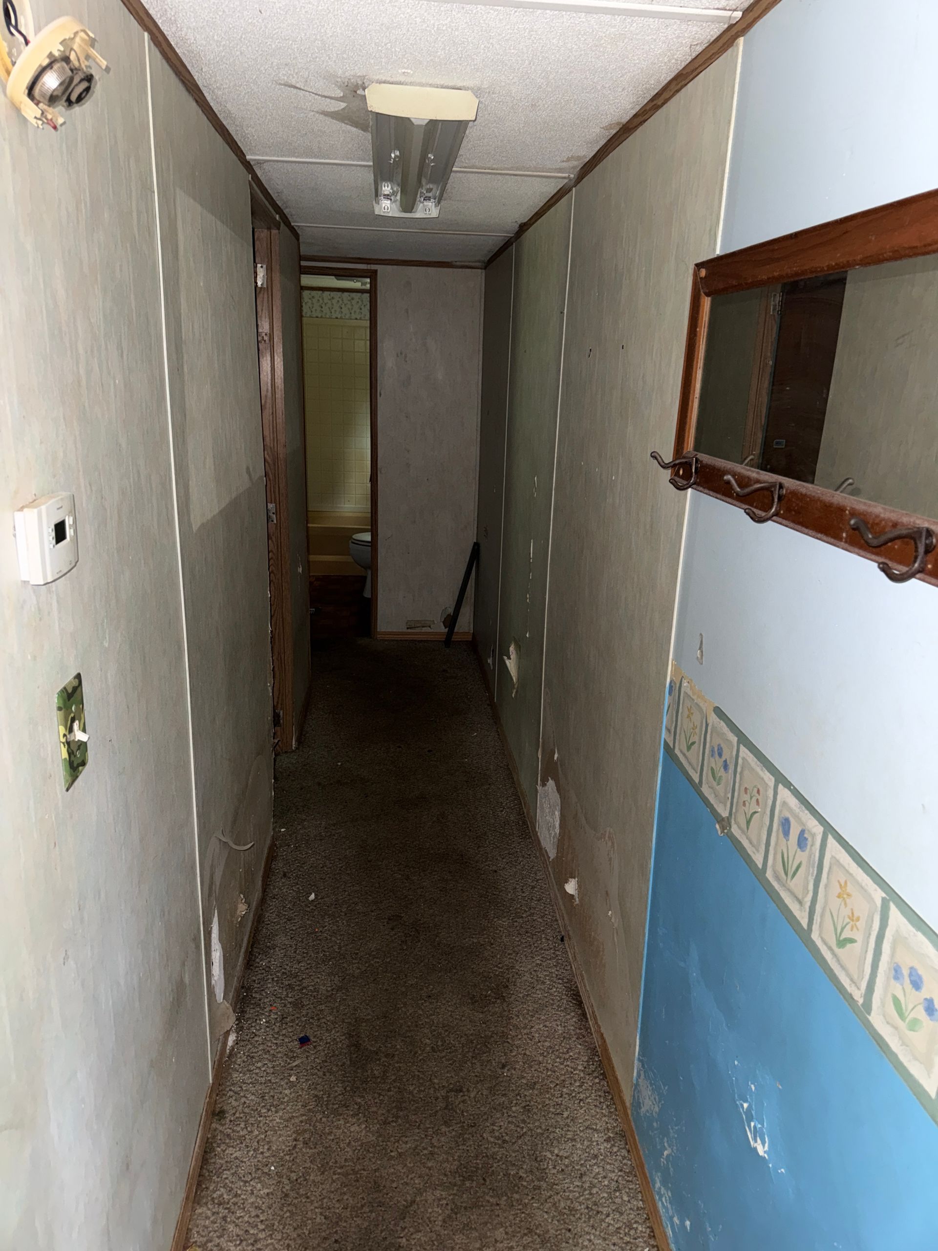 Narrow hallway with walls, a carpeted floor, and a doorway at the end.