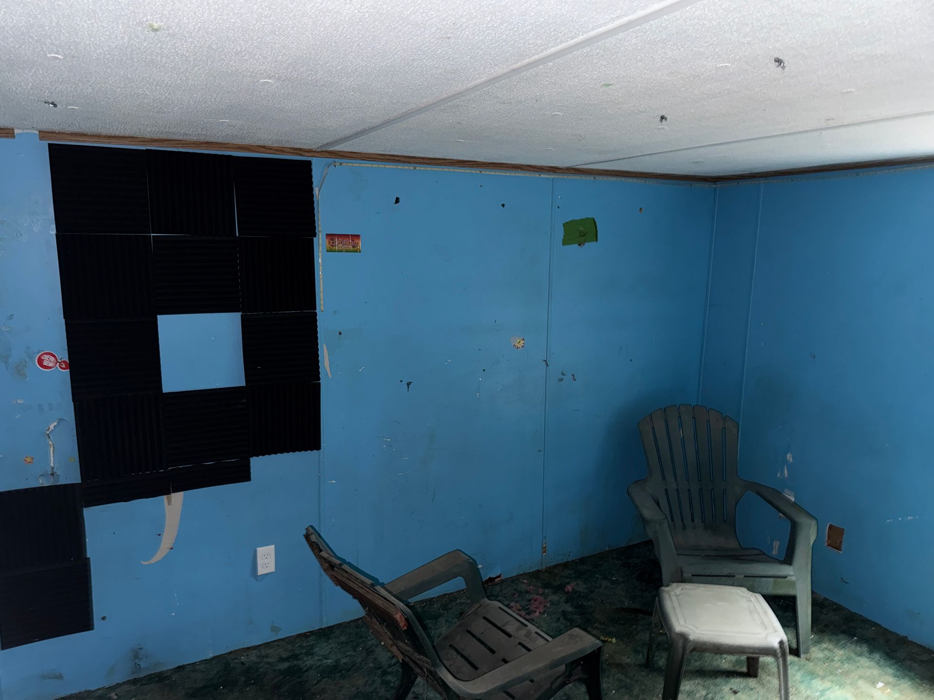 Blue-walled room with two chairs, and a small stool on a bare floor.