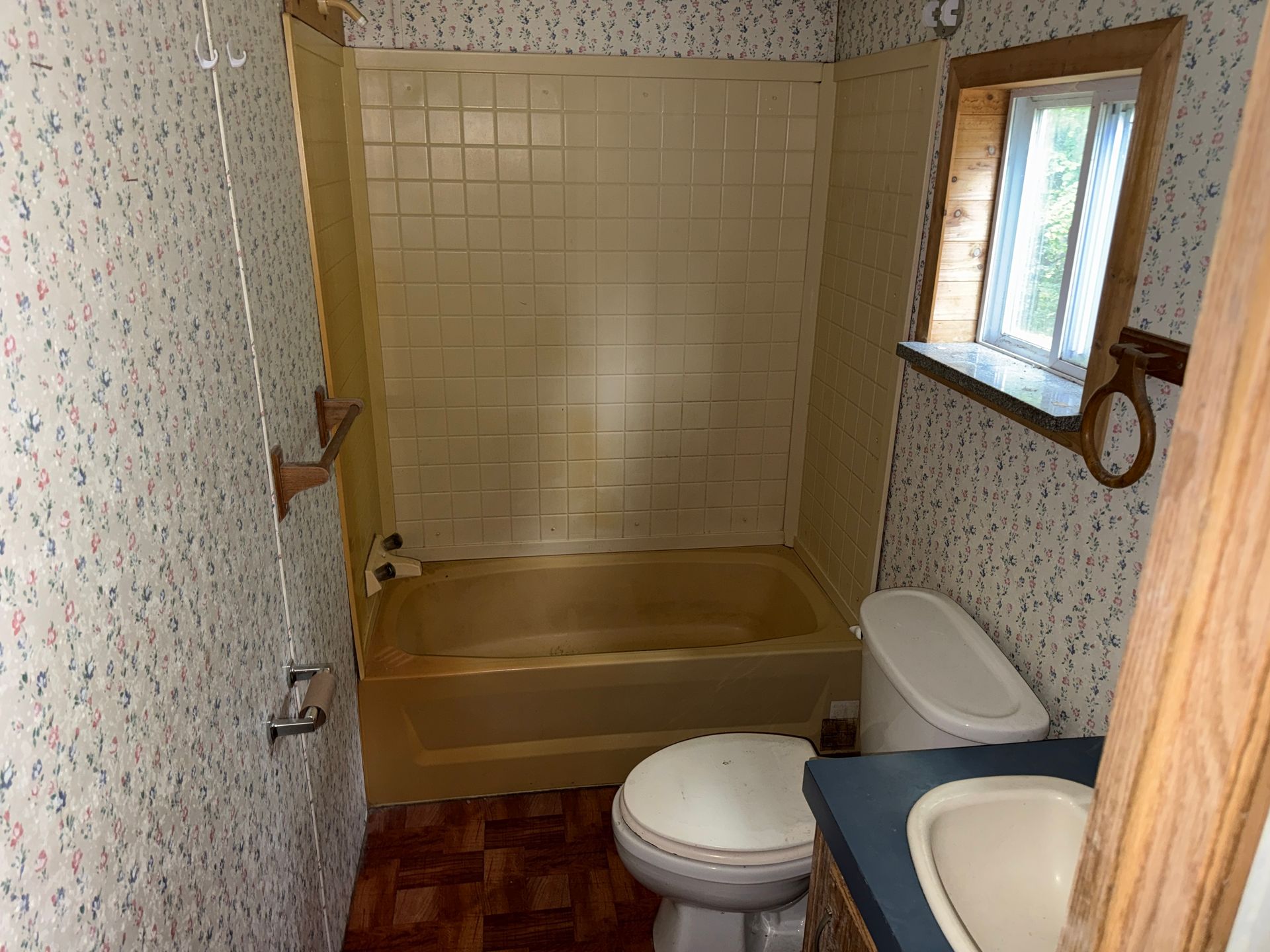 Small bathroom with a bathtub, toilet, sink, window, and floral wallpaper.
