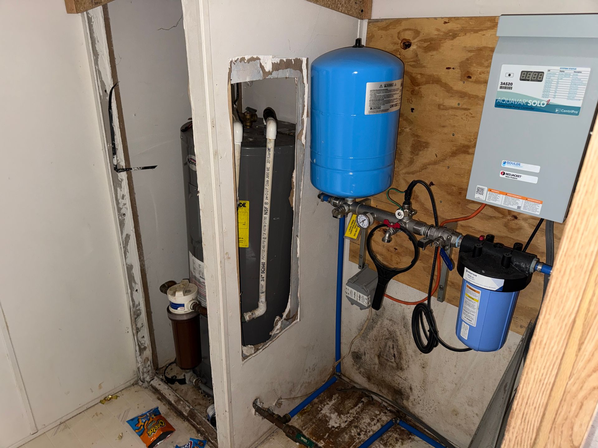 Utility closet with water filtration equipment, blue tanks, pipes, and an open wall panel