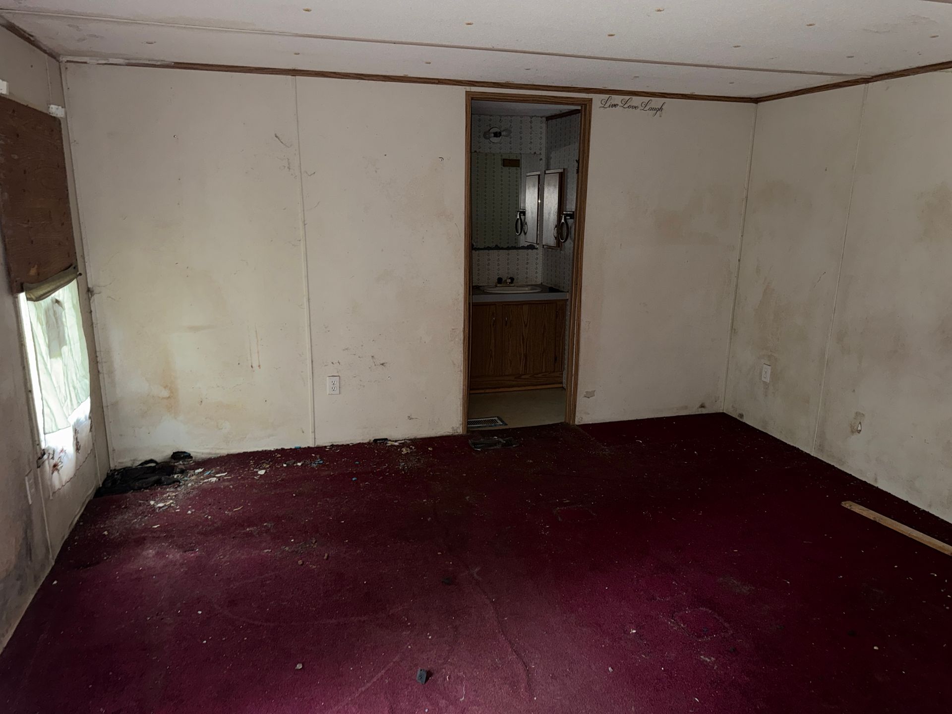 Empty room with white walls, burgundy carpet, and a doorway opening to a small kitchen.