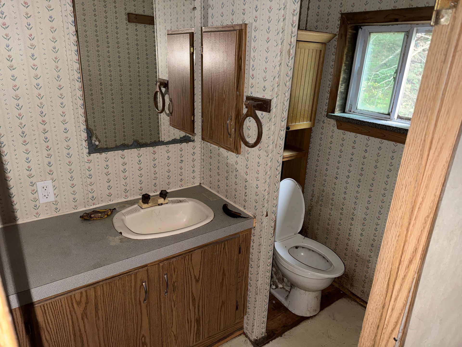 Small bathroom with sink, mirror, toilet, gray countertop, and a window on the right.