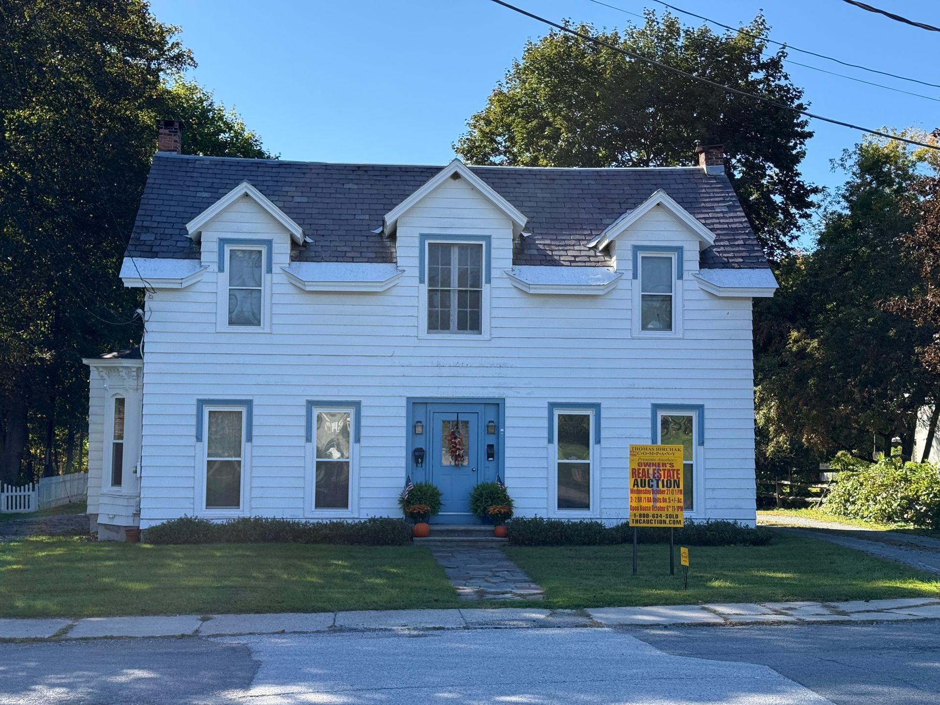 White two-story house with blue shutters and a front lawn, seen from the street