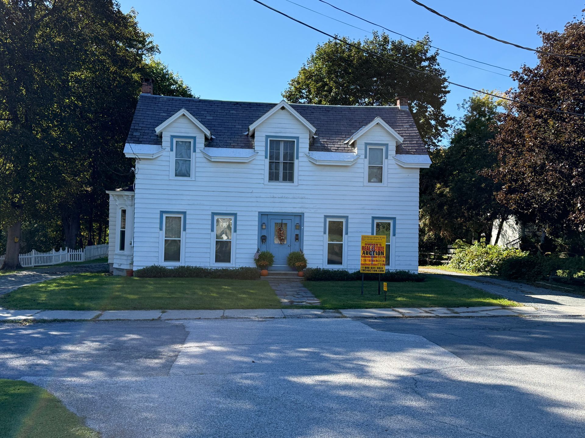 White two-story house with dormer windows, a front porch, and a brick walkway under a blue sky.