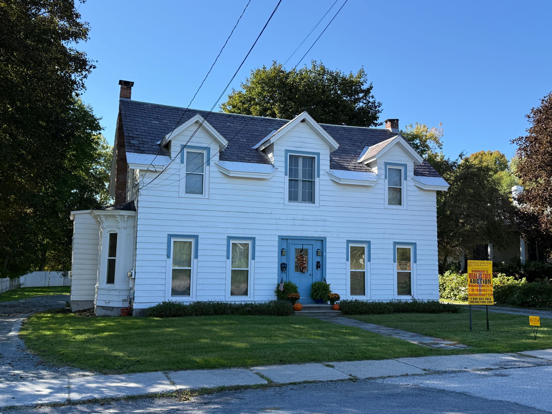 White two-story house with blue trim, front lawn, and a sign in the yard on a sunny day