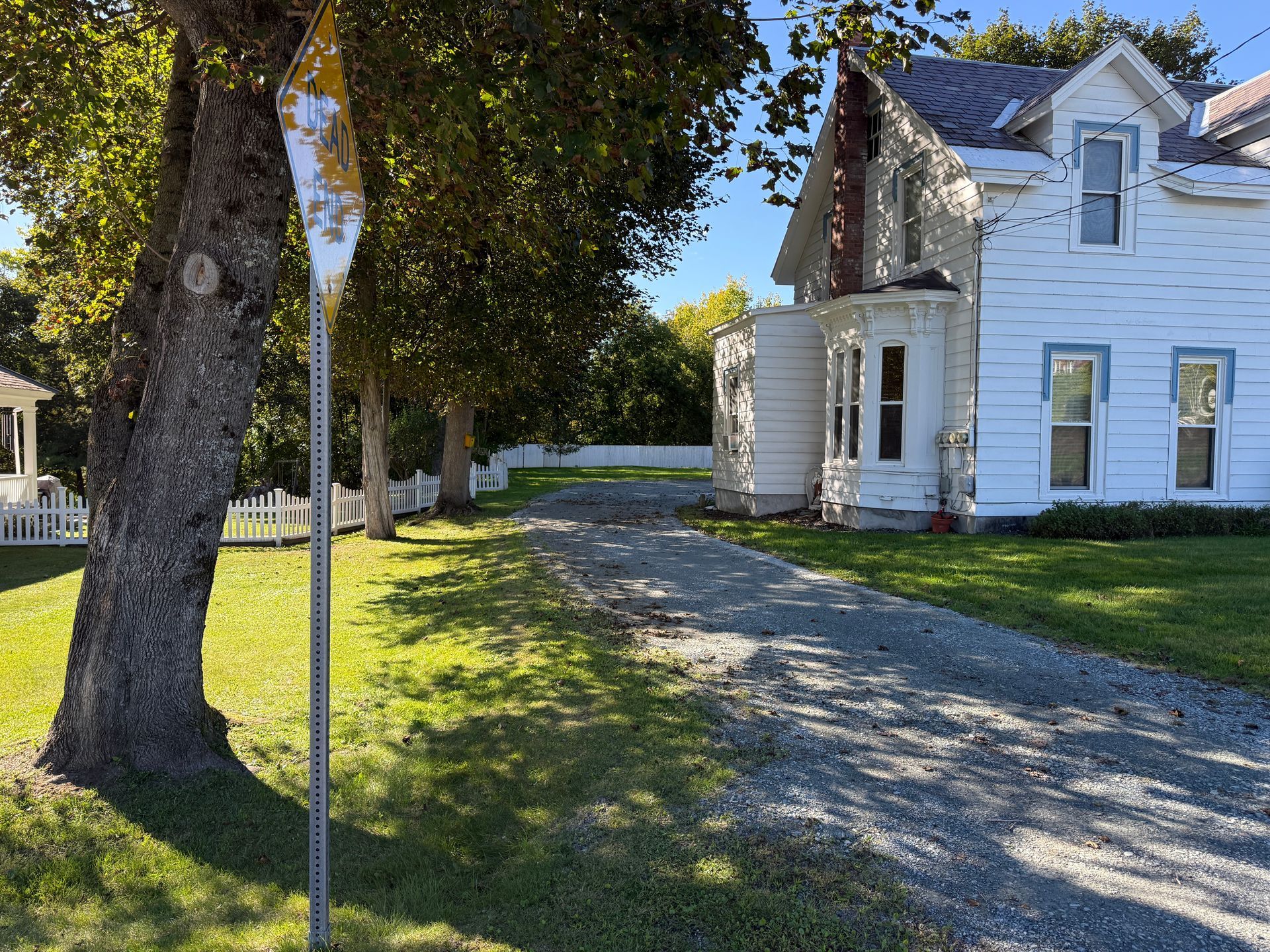 White house with gravel driveway and large trees in a sunny yard