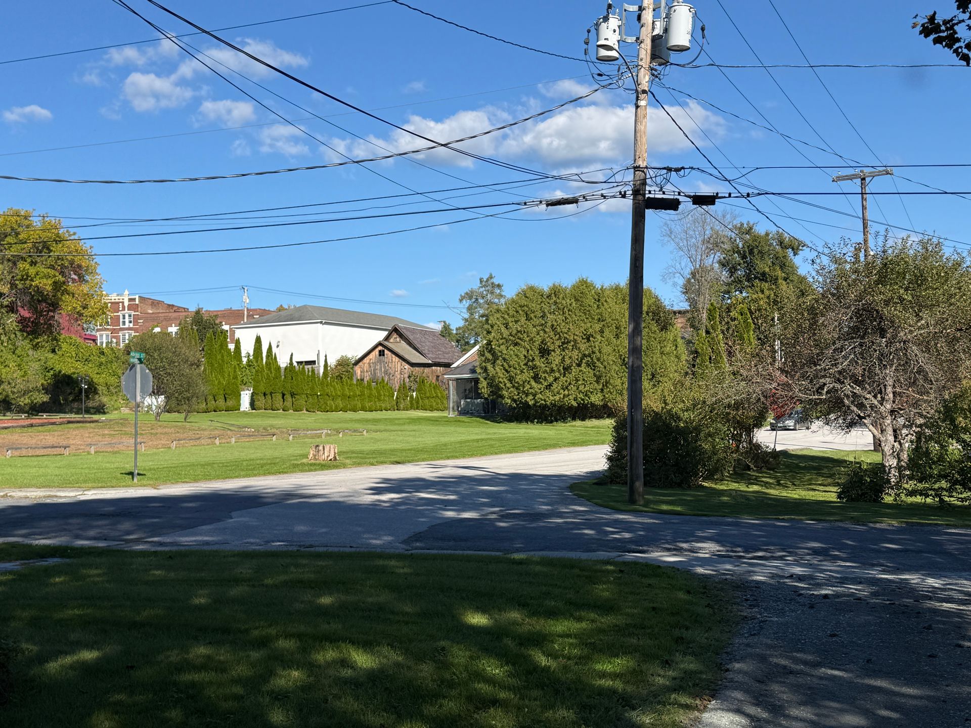 Residential street with utility pole, power lines, trees, and houses under a clear blue sky