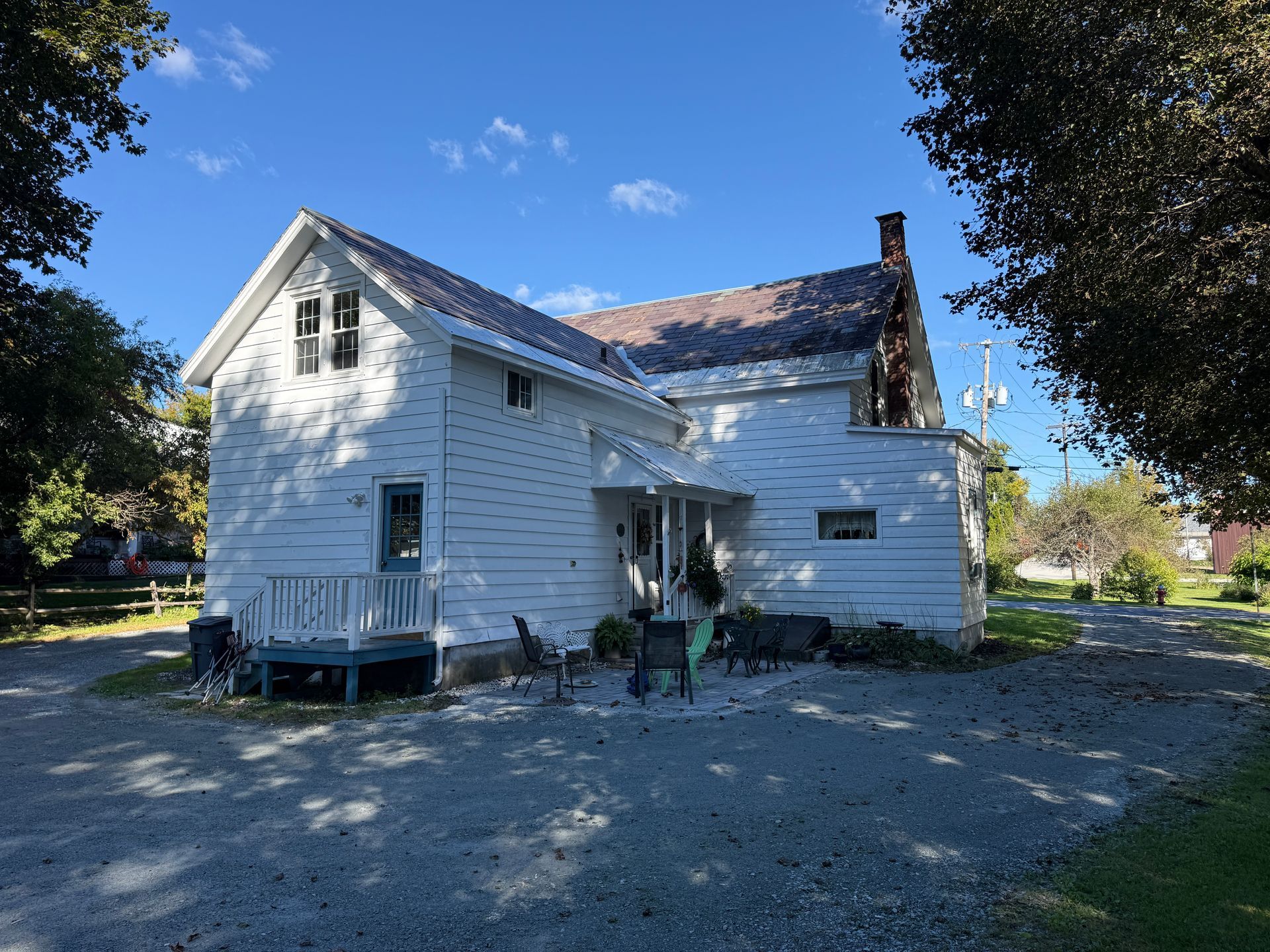 White two-story house with siding, gravel yard, and blue sky trees surrounding it
