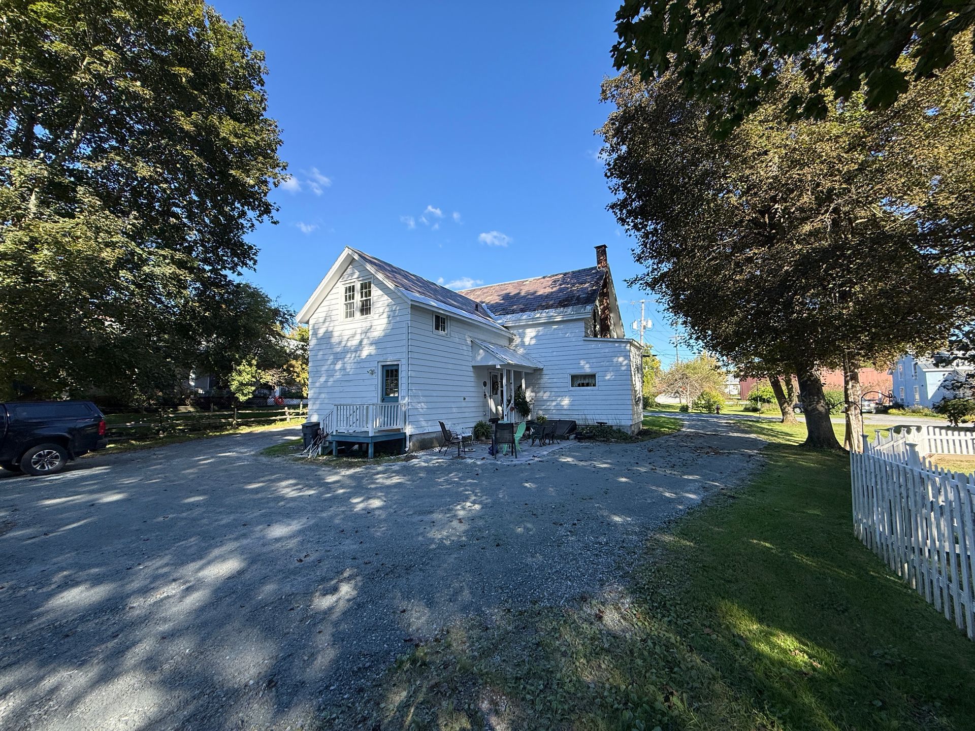 White house on a gravel driveway with trees and a white fence in bright sunlight