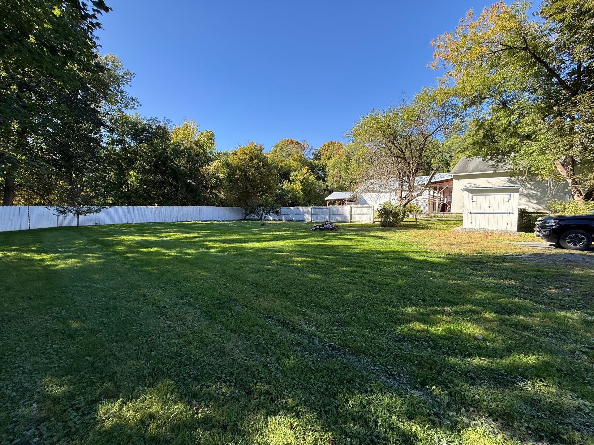 Grassy backyard with white fence, trees, and a small shed under a blue sky