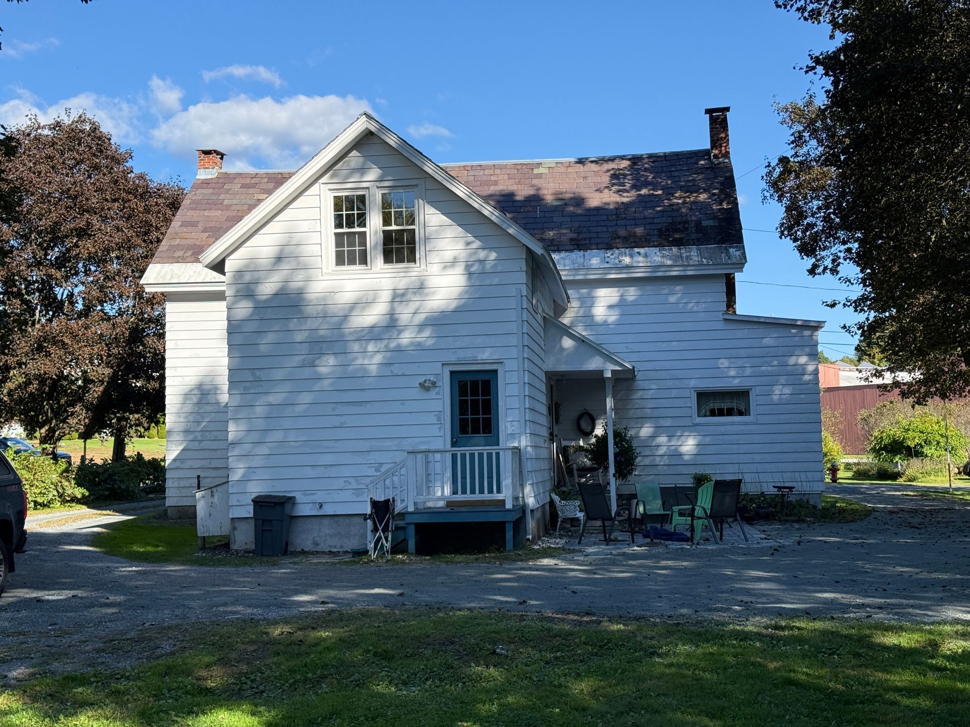 White two-story house with porch and gravel yard on a sunny day