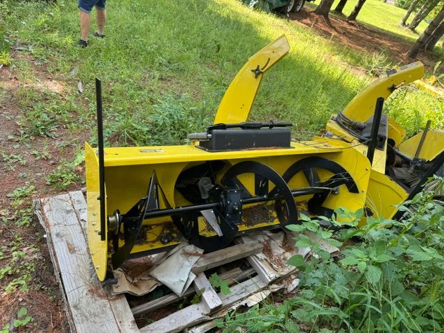 Yellow snowblower on a wooden pallet in a grassy yard