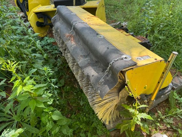 Yellow brush mower attachment clearing weeds along a grassy path
