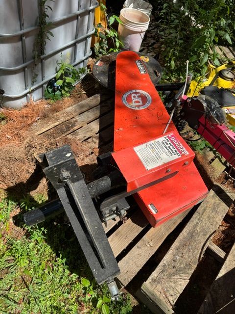 Red metal mower deck attachment on a wooden pallet in a grassy yard