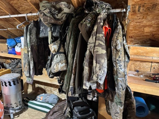 Camouflage jackets and outdoor gear hanging inside a rustic wooden shed
