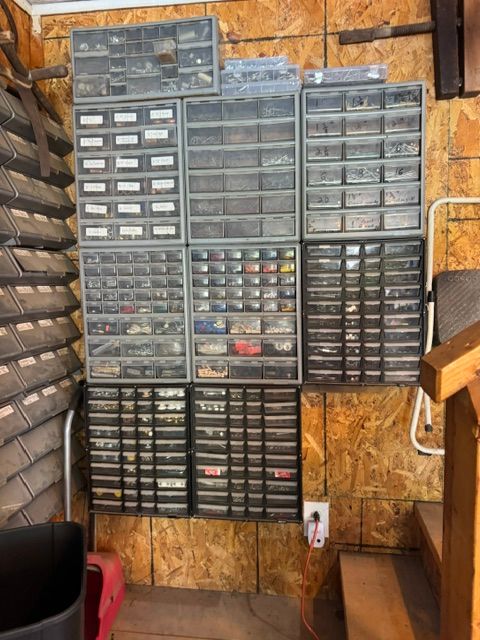 Wall of organized plastic parts drawers in a workshop, mounted on OSB wood panels.