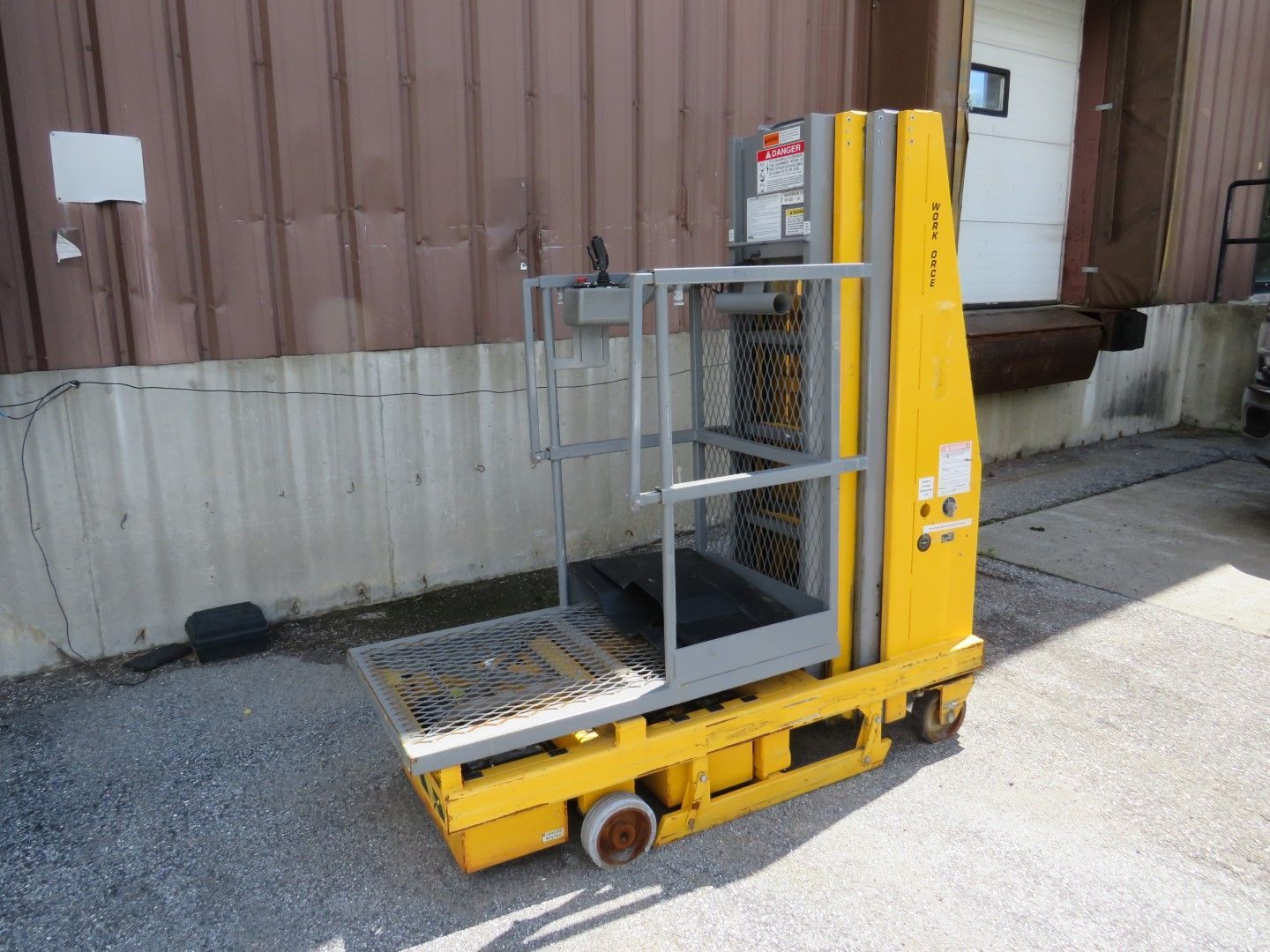 Yellow industrial lift platform with safety cage, parked outside a loading dock.