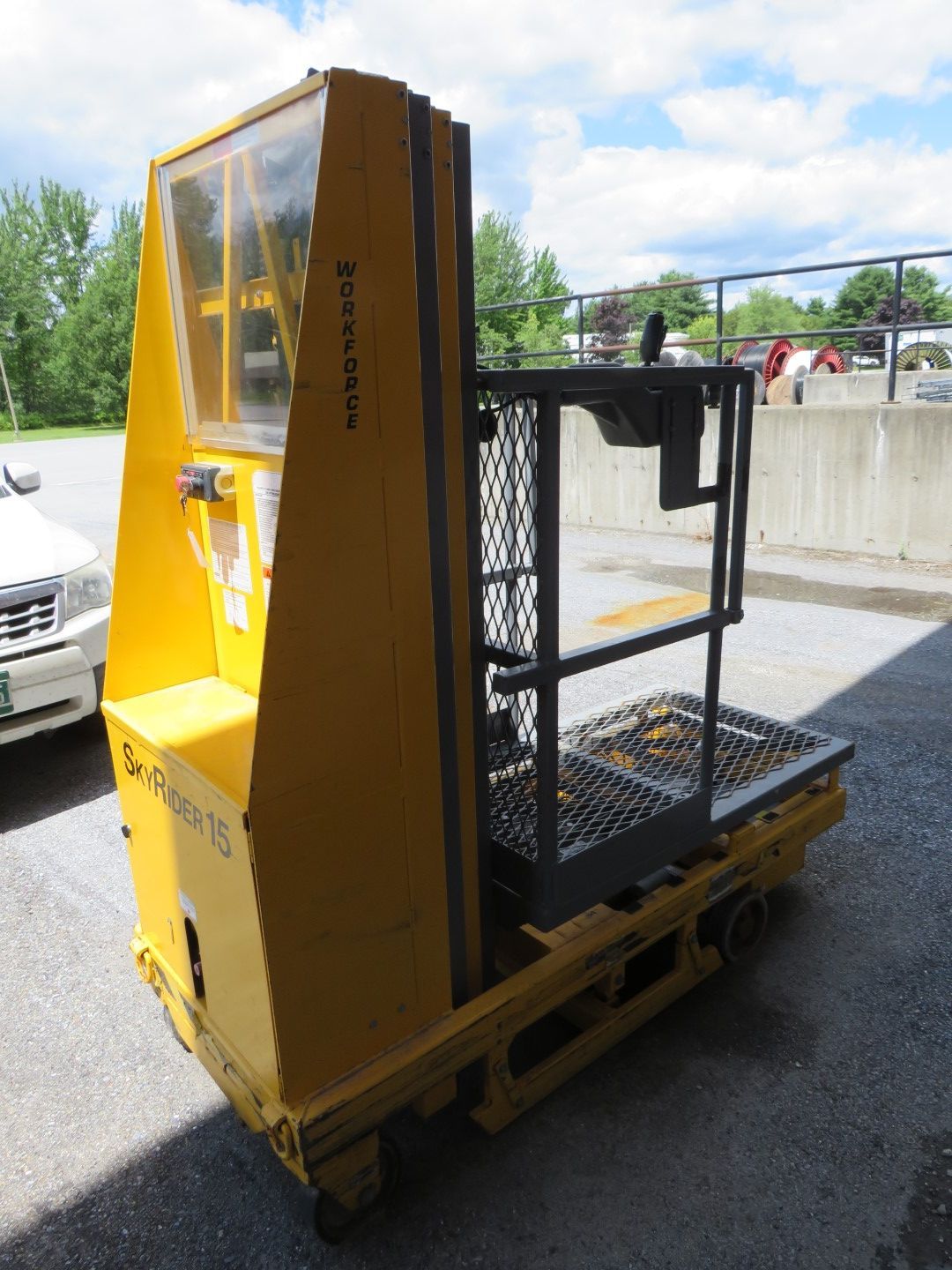 Yellow industrial lift with open platform and protective cage, parked outside.