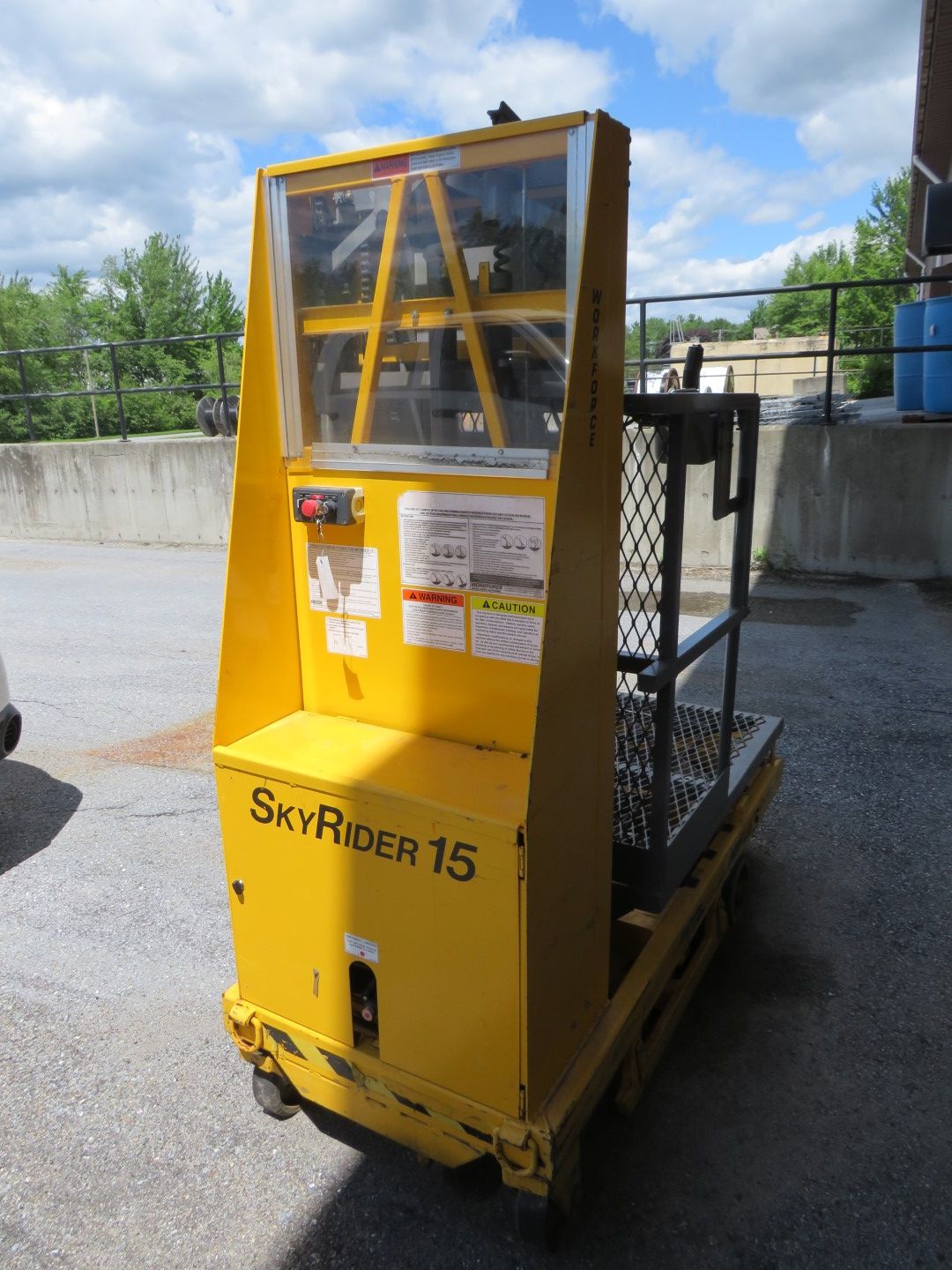 Yellow SkyRider 15 aerial lift on wheels, outdoors near a loading dock.