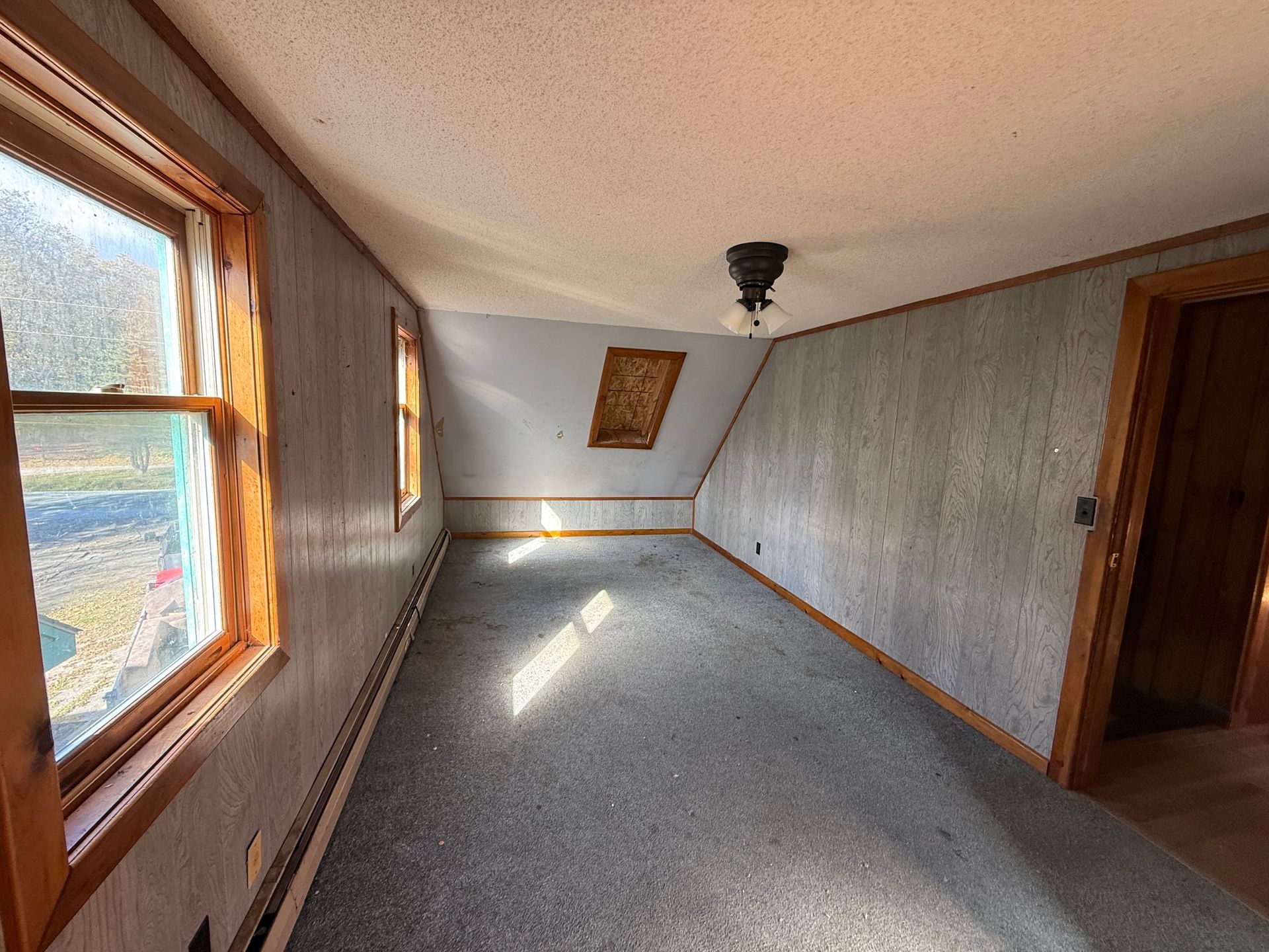 Empty narrow hallway with gray walls, wood-trimmed windows, and sunlight on a speckled floor