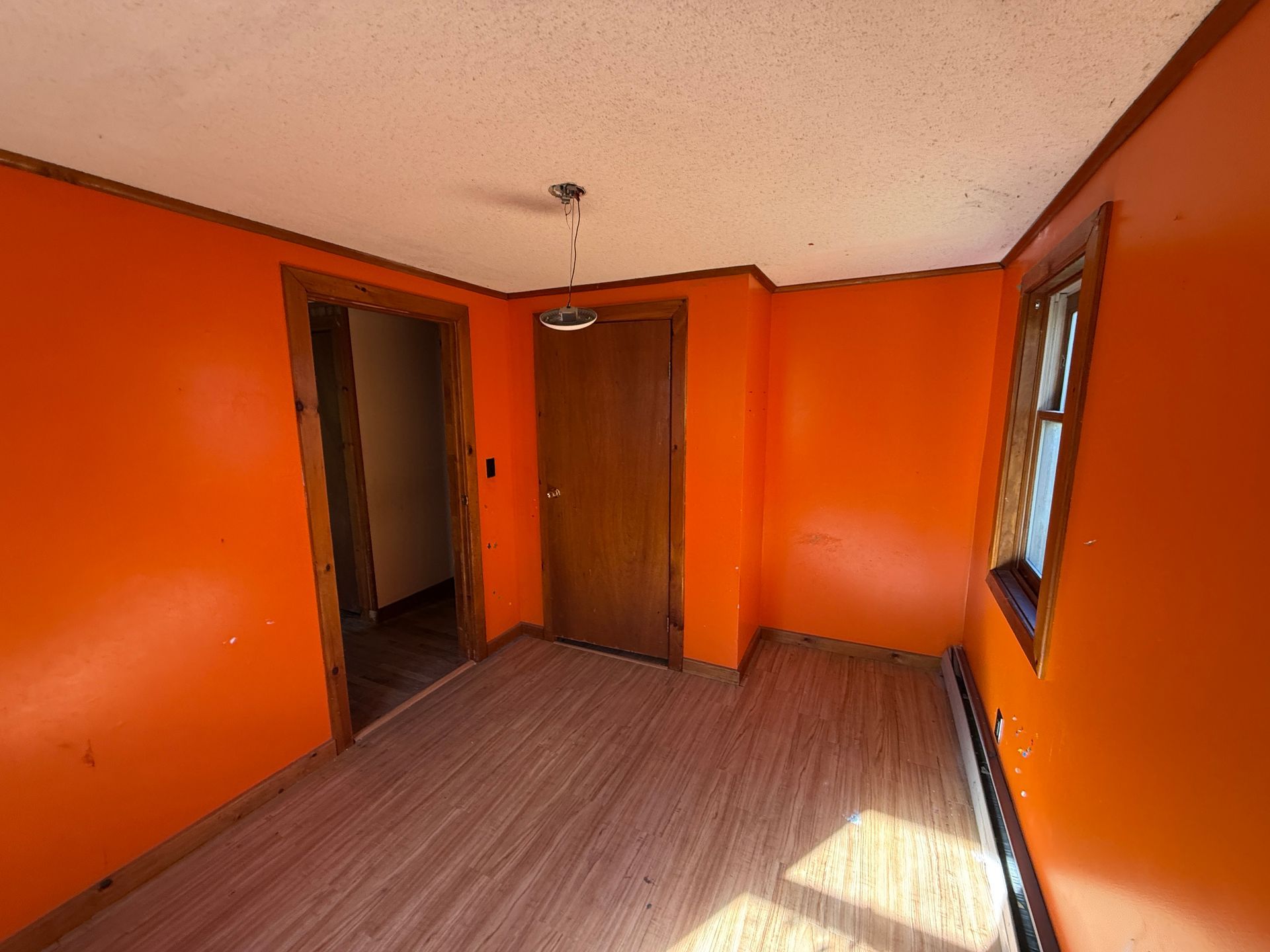 Empty orange room with wood floor, two doors, and a small window.